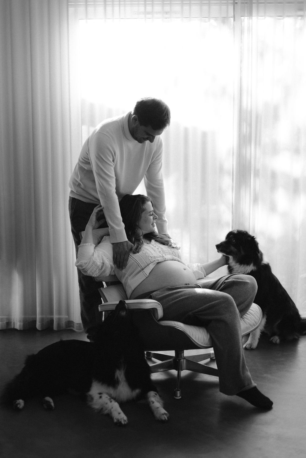 Black and white photo series of a couple sitting with their dog in a bright room with curtains.