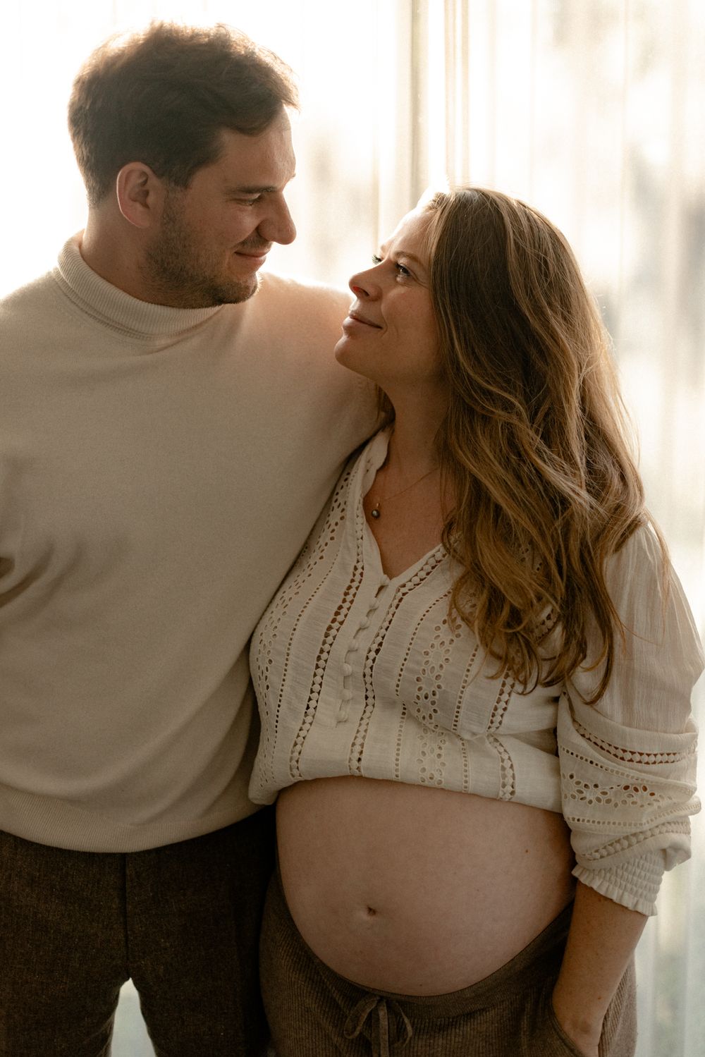 A loving couple shares an intimate moment during a maternity photoshoot with soft natural lighting.