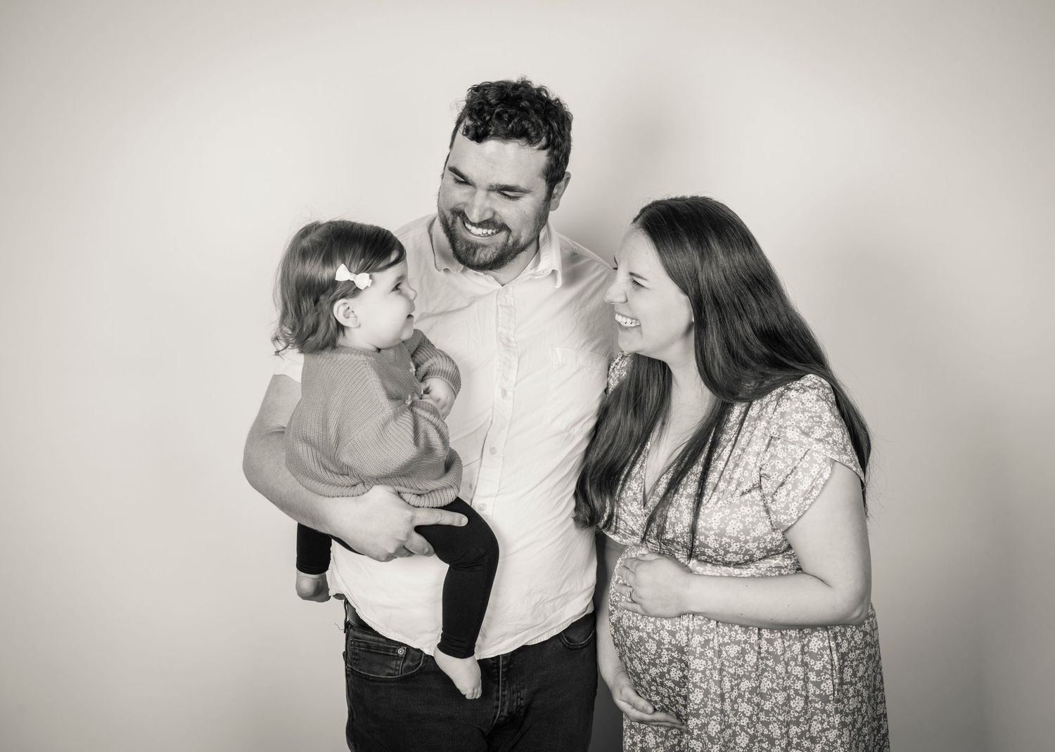 a family in a photo studio smile at their baby. the mother holds her pregnant belly