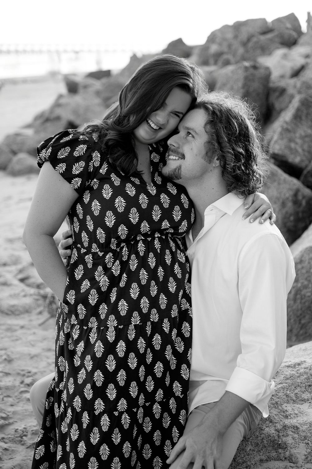 Black and white portrait of couple sharing tender moments among coastal rocks.