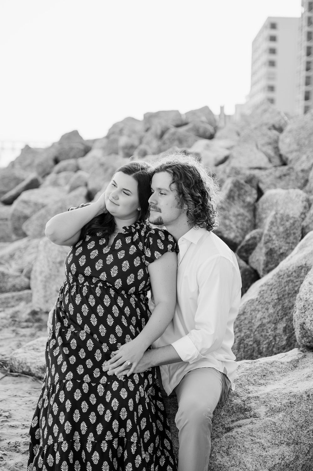 Black and white beach portrait of couple relaxing on rocky shoreline.