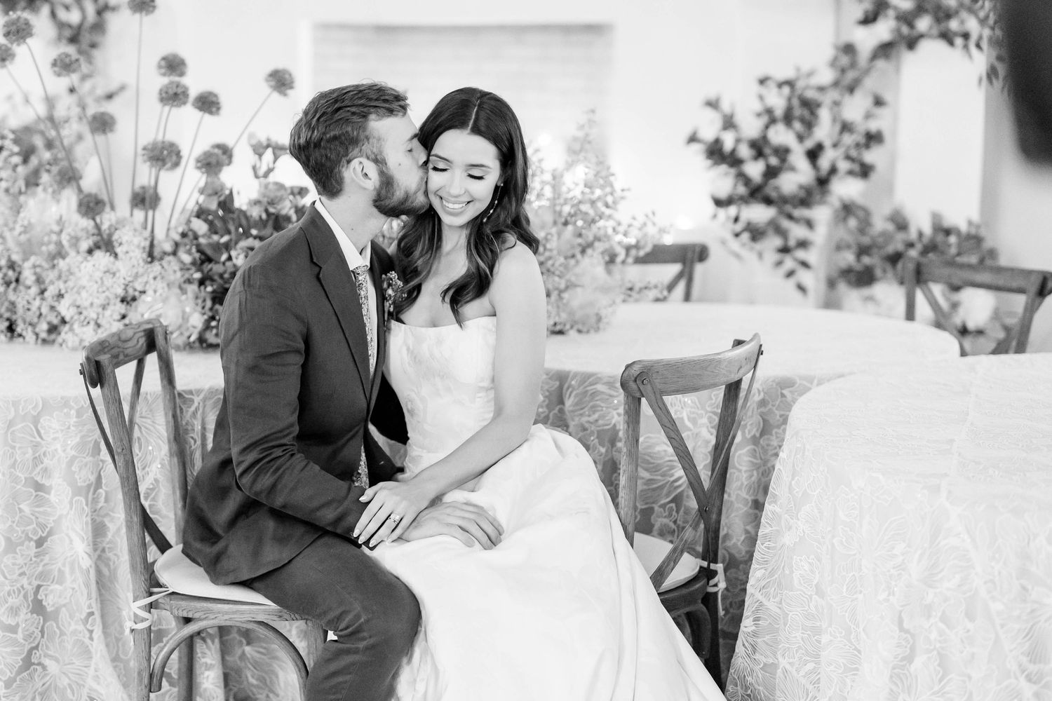 bride sits on groom's lap as he kisses her