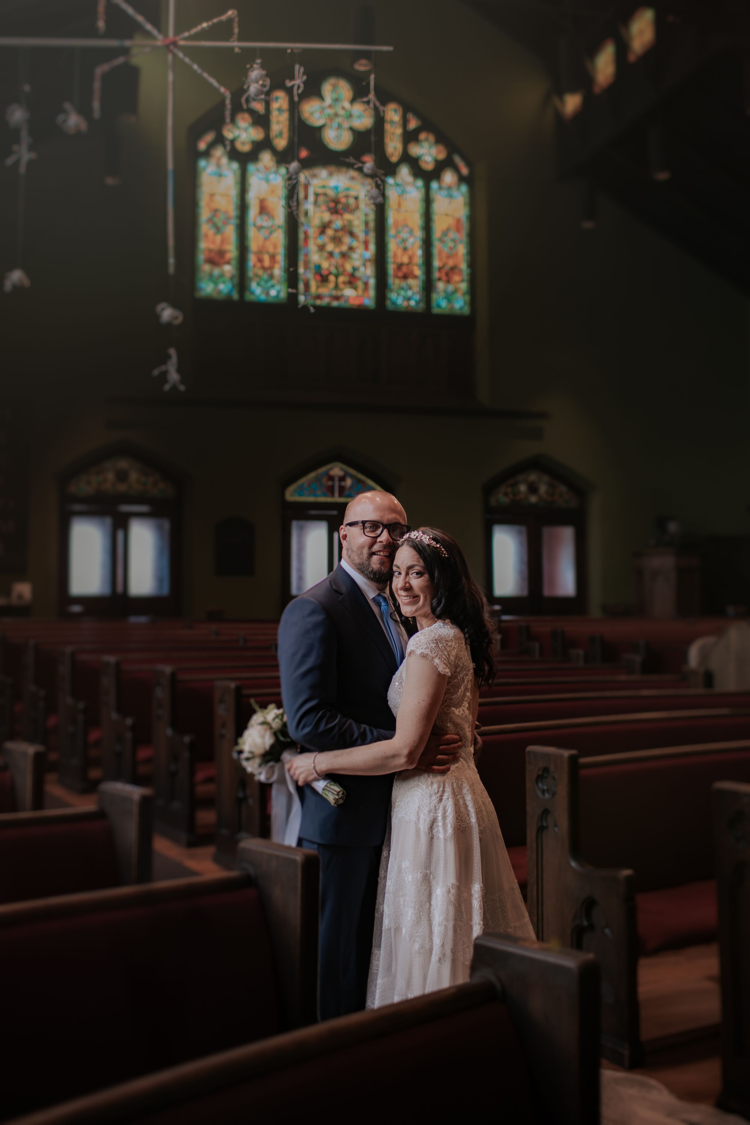 A couple shares an intimate moment in a dimly lit church with stained glass windows and wooden pews.