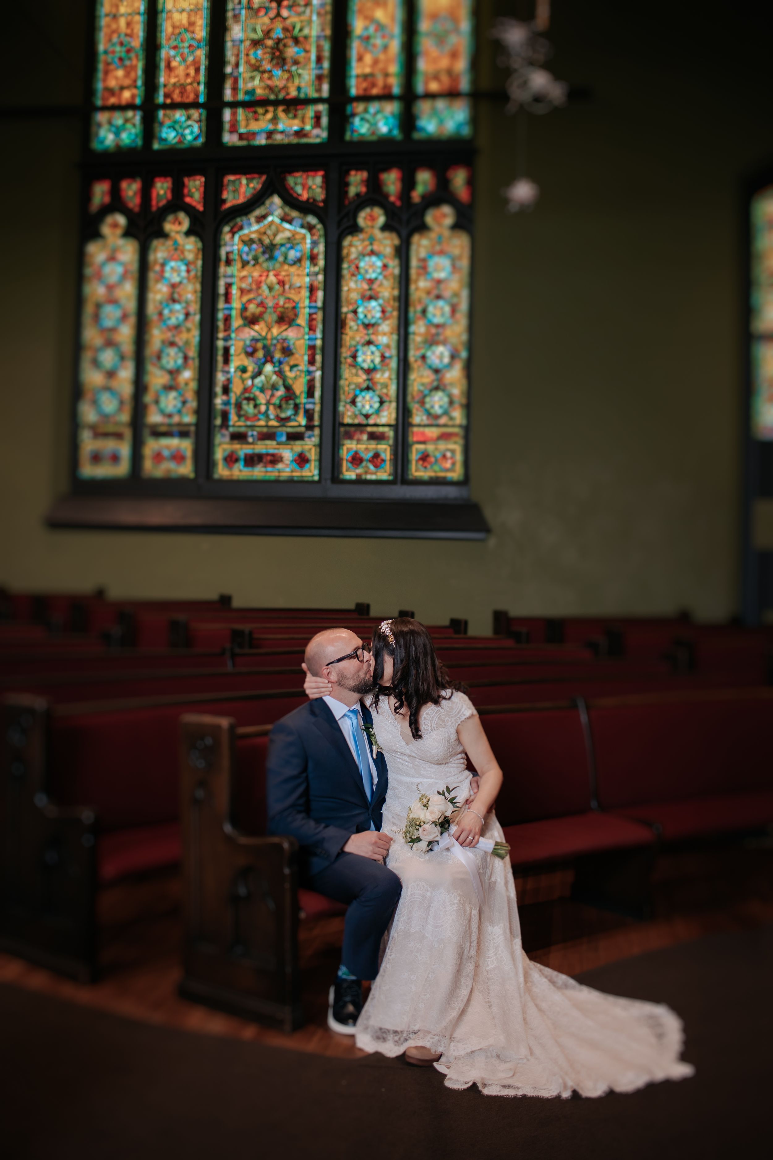 A romantic moment in a church sanctuary with ornate stained glass windows and wooden pews.