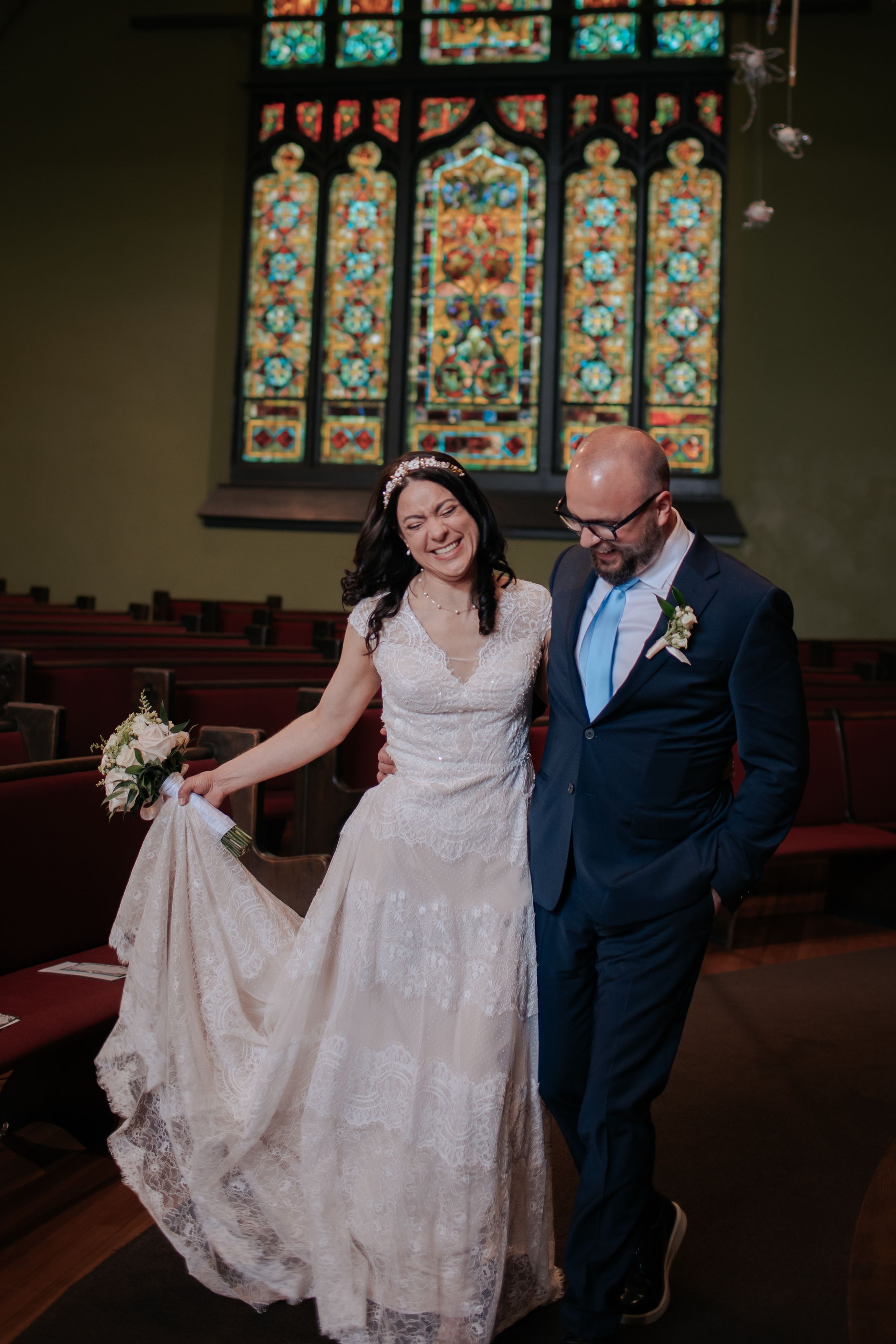 A couple shares a joyful moment in a church with beautiful stained glass windows and ornate decor in the background.