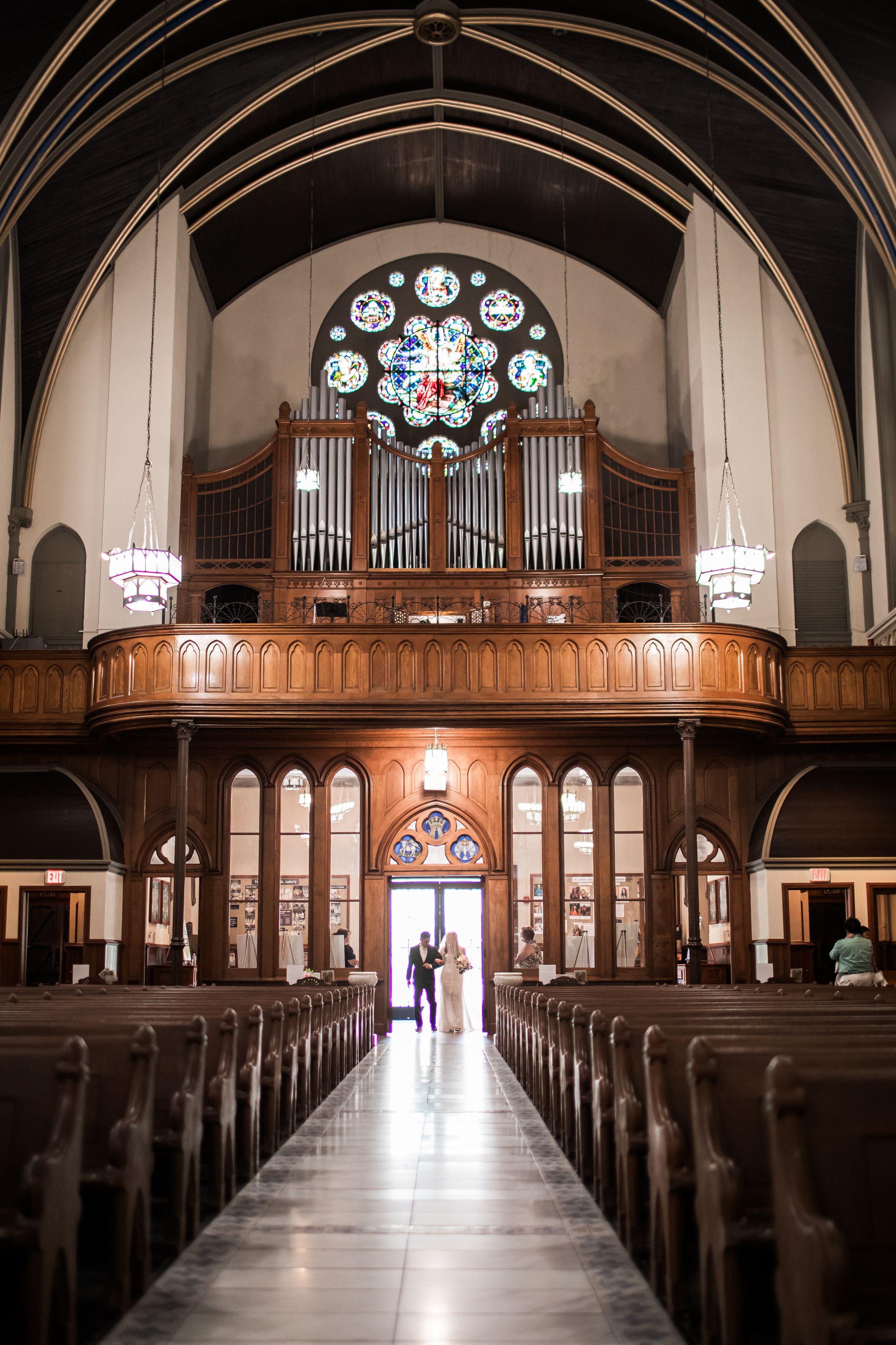 Interior of a church with wooden pews leading to a grand pipe organ and stained glass rose window above.