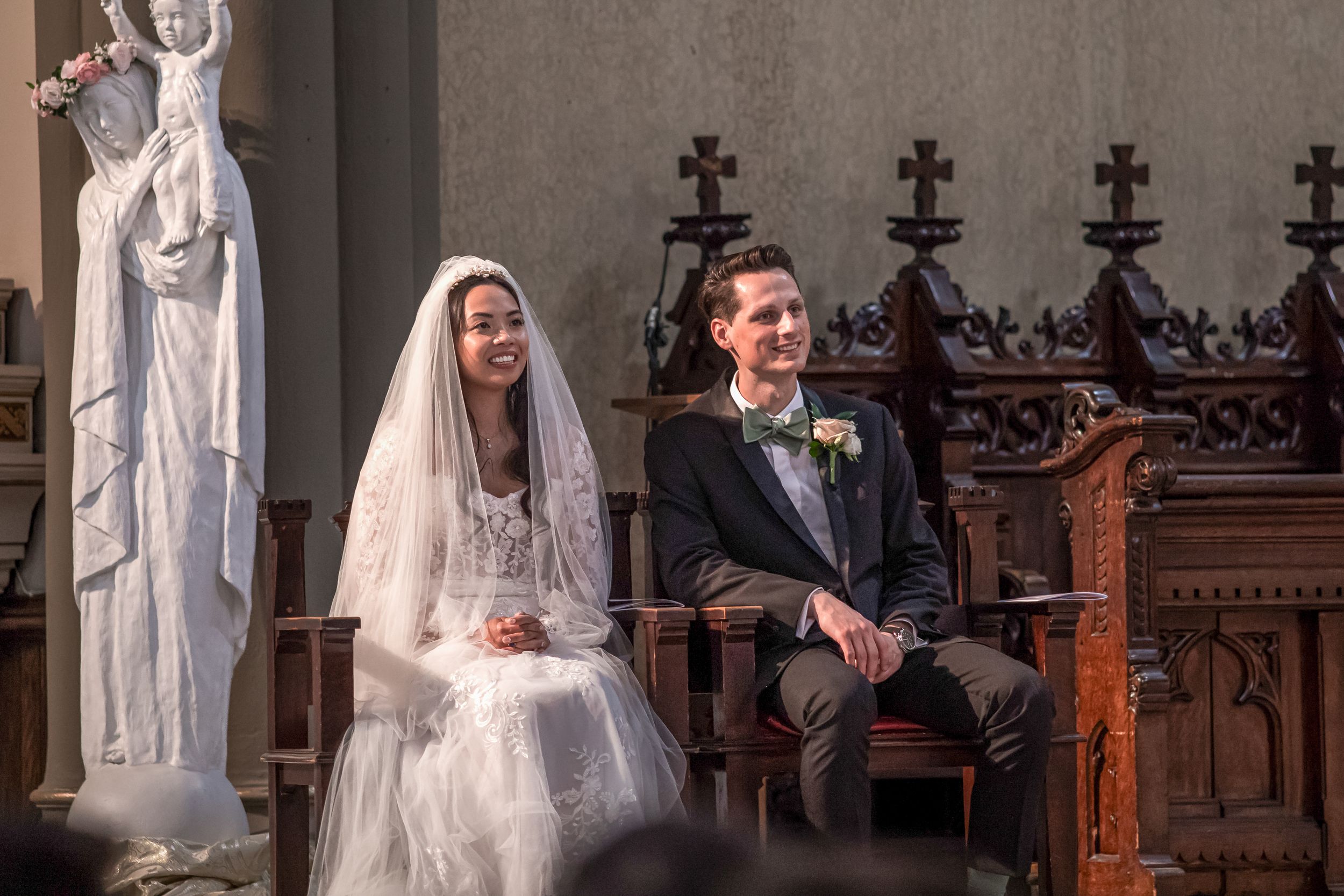 A wedding ceremony takes place in a traditional church with ornate wooden pews and decorative gothic details.
