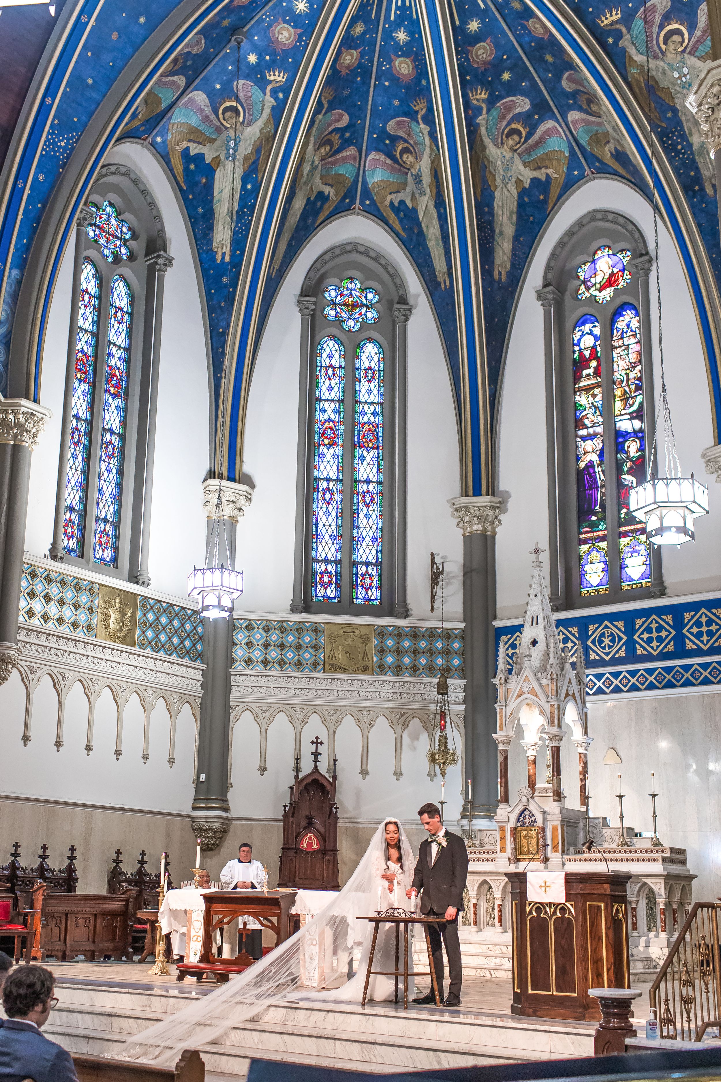 Interior panorama of a Gothic church sanctuary with blue vaulted ceilings, stained glass windows and ornate altar area.