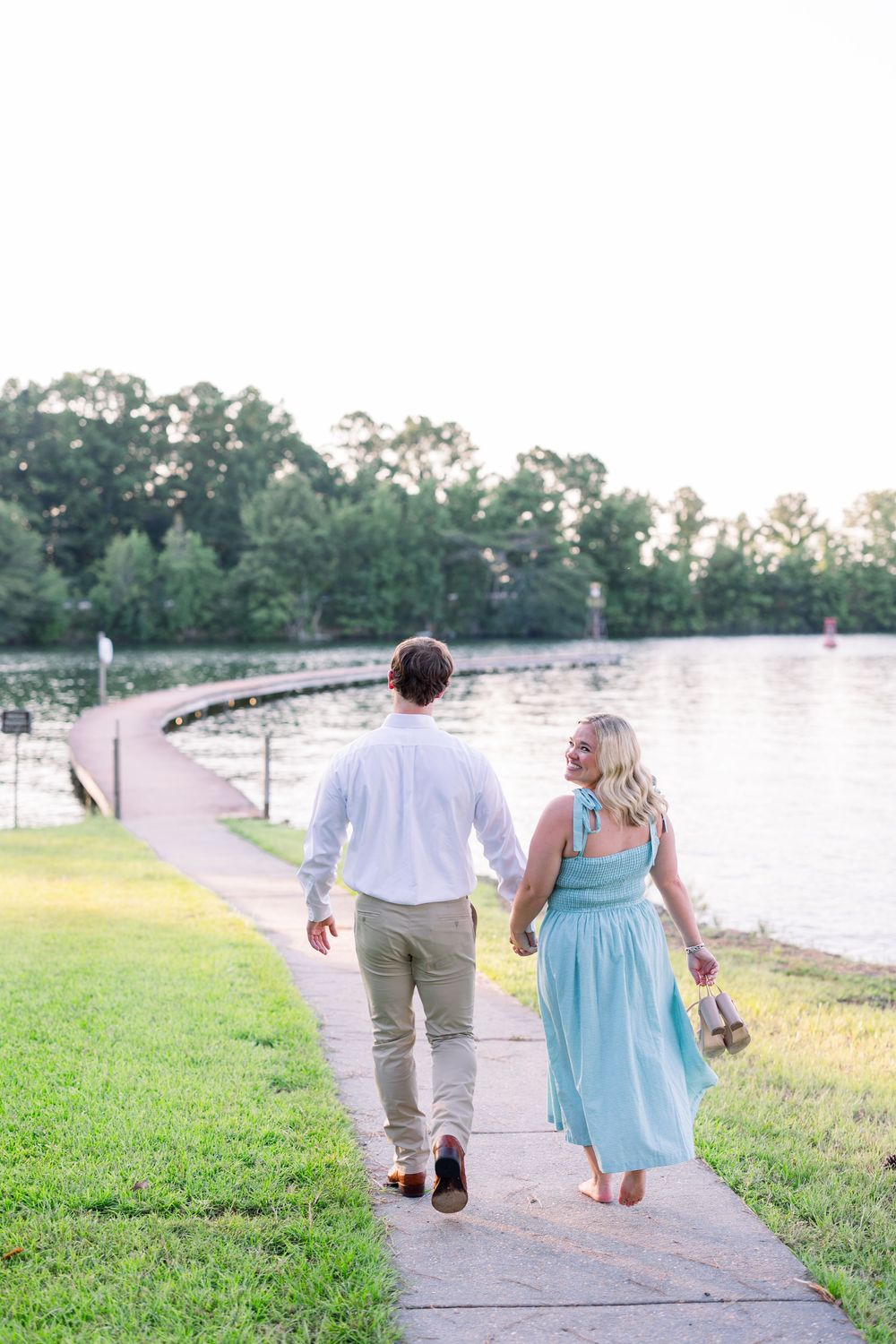 A couple walks hand in hand along a lakeside path at sunset in matching blue and white outfits.