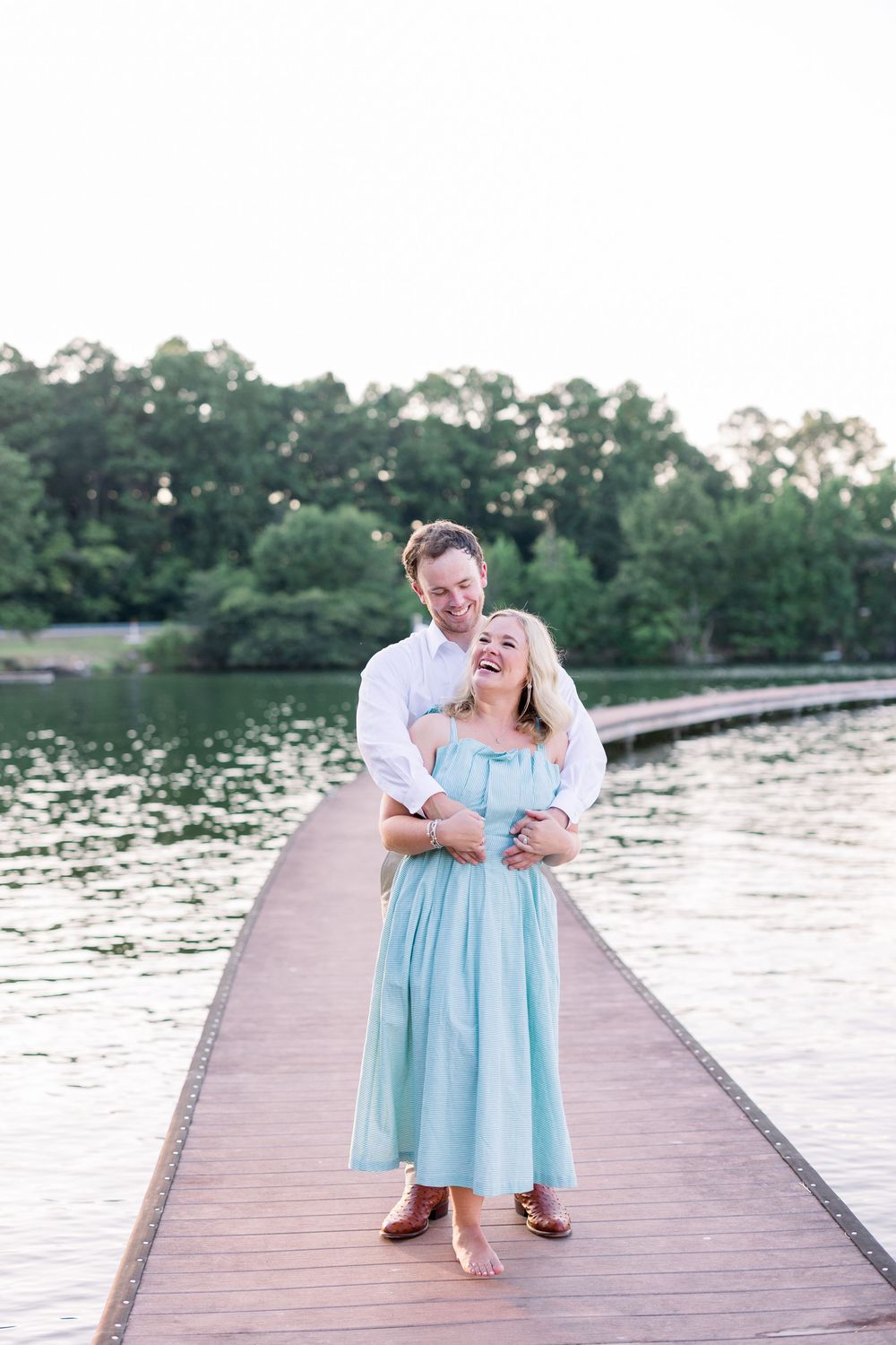 A couple shares a romantic moment on a wooden dock by a serene lake during sunset.