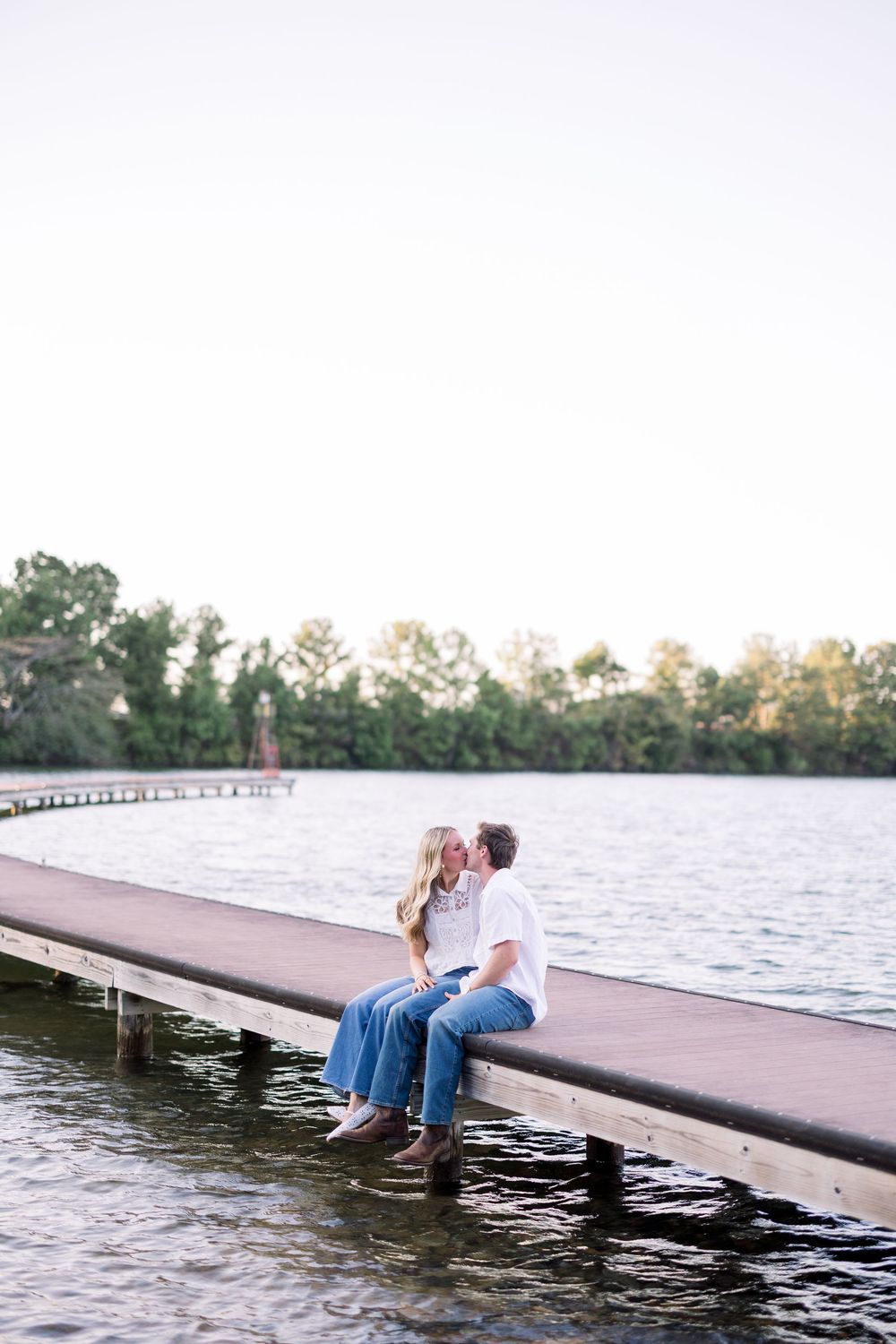 Couple relaxing on wooden dock by lake at sunset enjoying peaceful moment together.