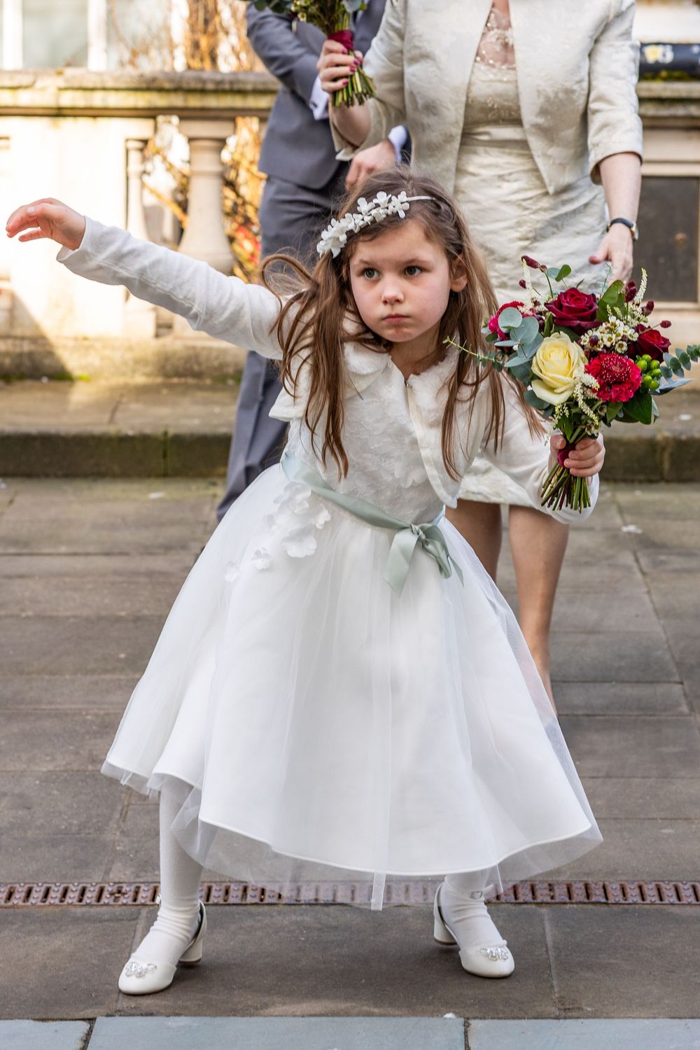 Flower girl strikes a pose in white dress holding a bouquet outside Southport Town Hall during a relaxed wedding arrival moment.