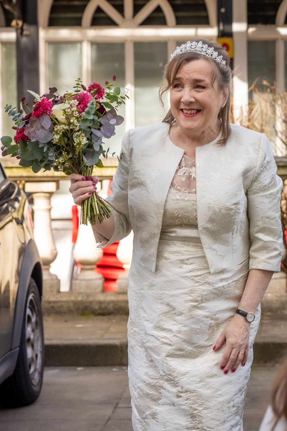 Bride holding bouquet outside Southport Town Hall, smiling in ivory dress and jacket before wedding ceremony.