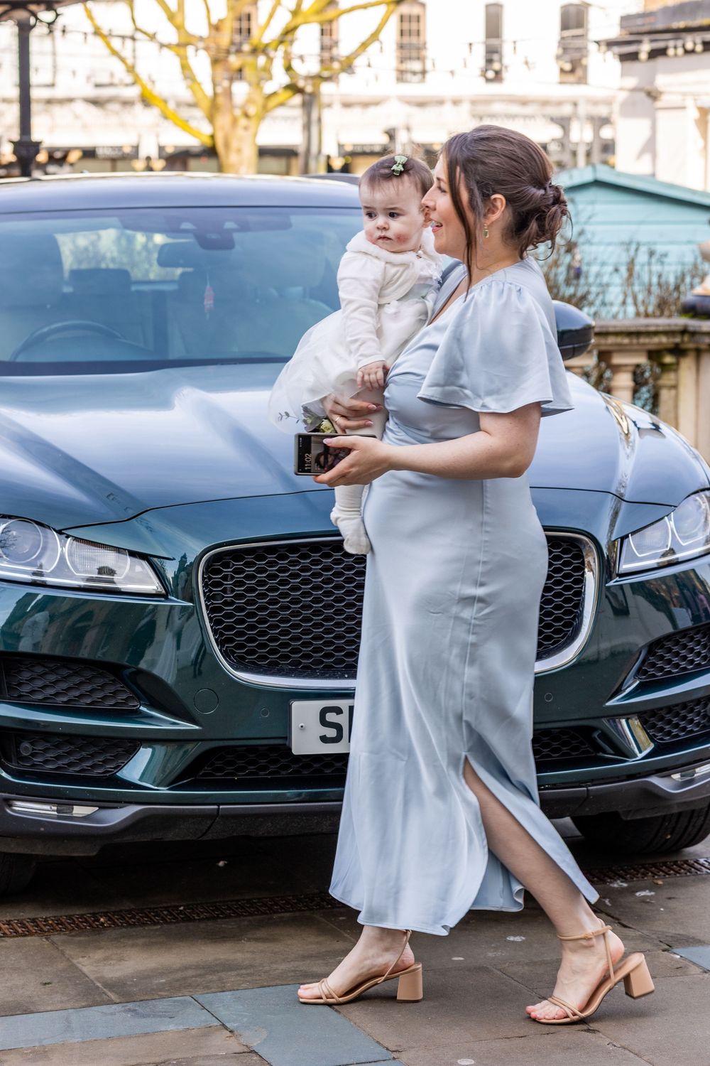 Bridesmaid holding baby daughter in front of wedding car outside Southport Town Hall, candid moment before the ceremony.
