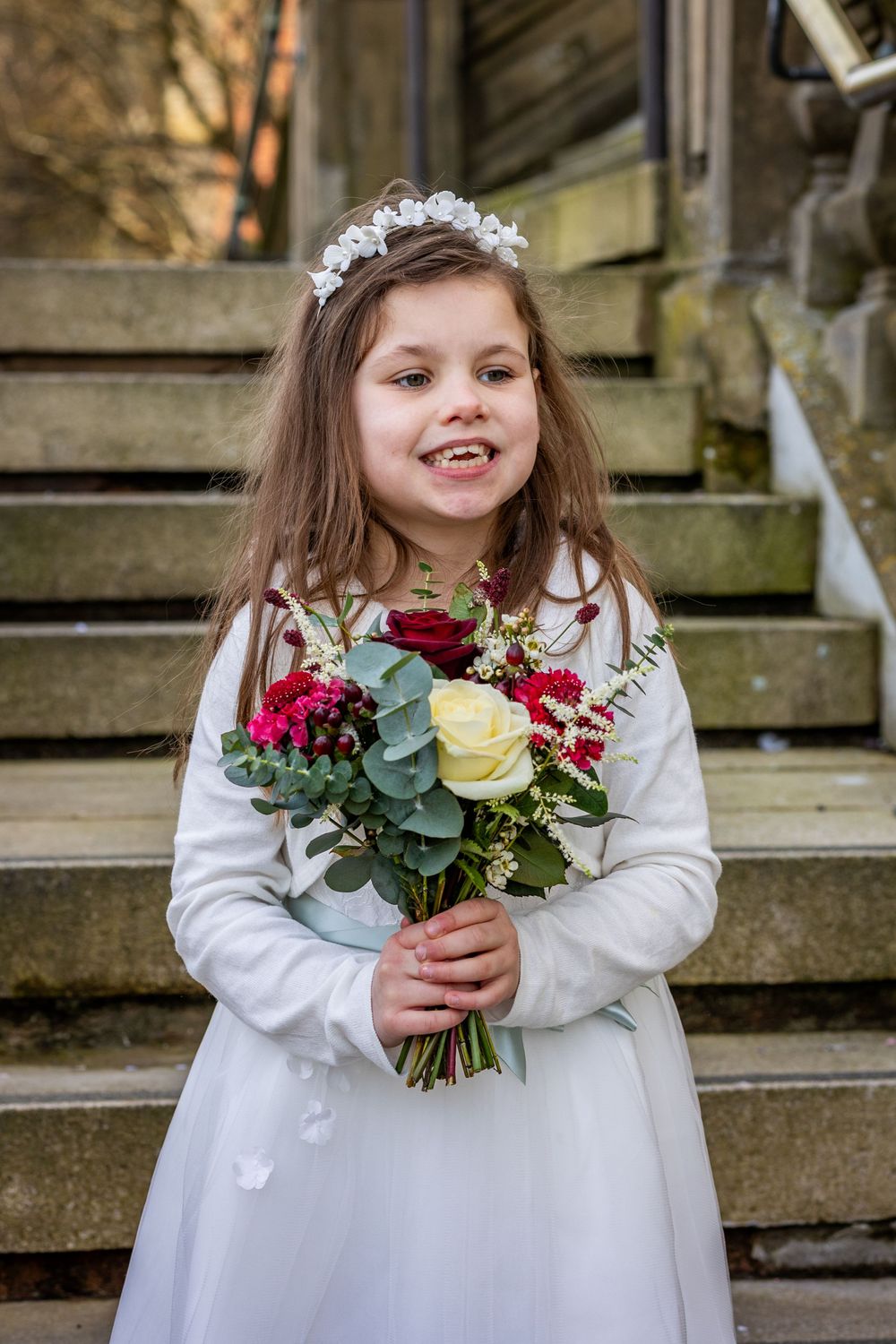 Flower girl holding bouquet on stone steps outside Southport Town Hall, smiling during relaxed wedding portraits