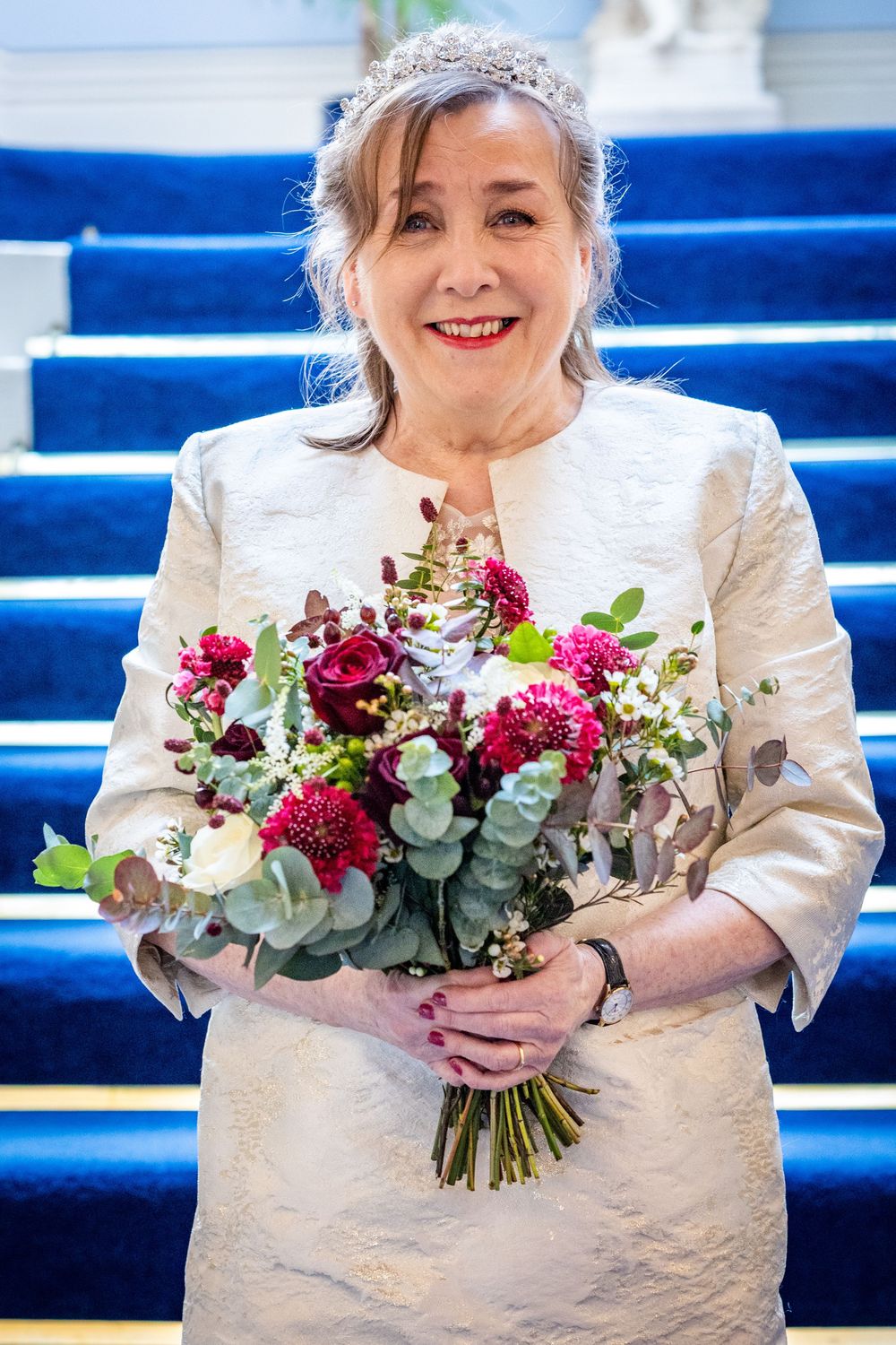 Bride smiling on blue staircase holding colourful bouquet at Southport Town Hall wedding ceremony in the North West UK