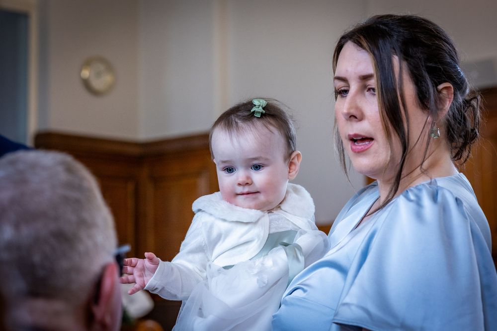 Bridesmaid holding baby in pale blue dress during Southport Town Hall wedding ceremony, natural candid moment in the North West