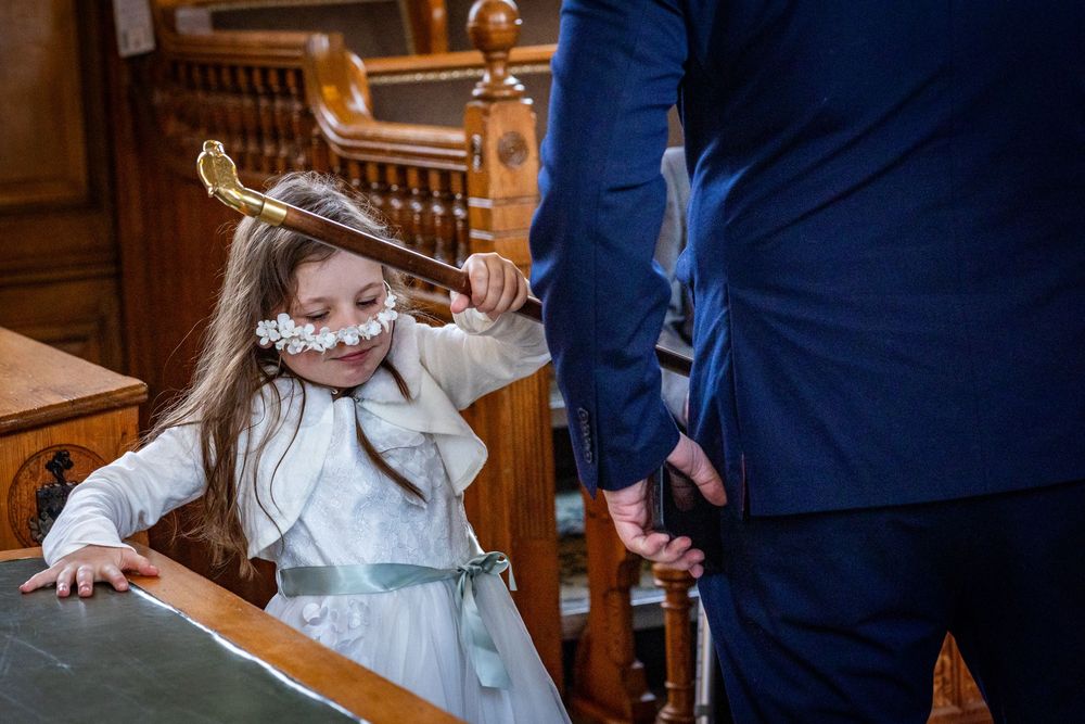 Flower girl plays with walking cane during Southport Town Hall wedding in Sefton, flower headband fallen over her eyes candid family moment