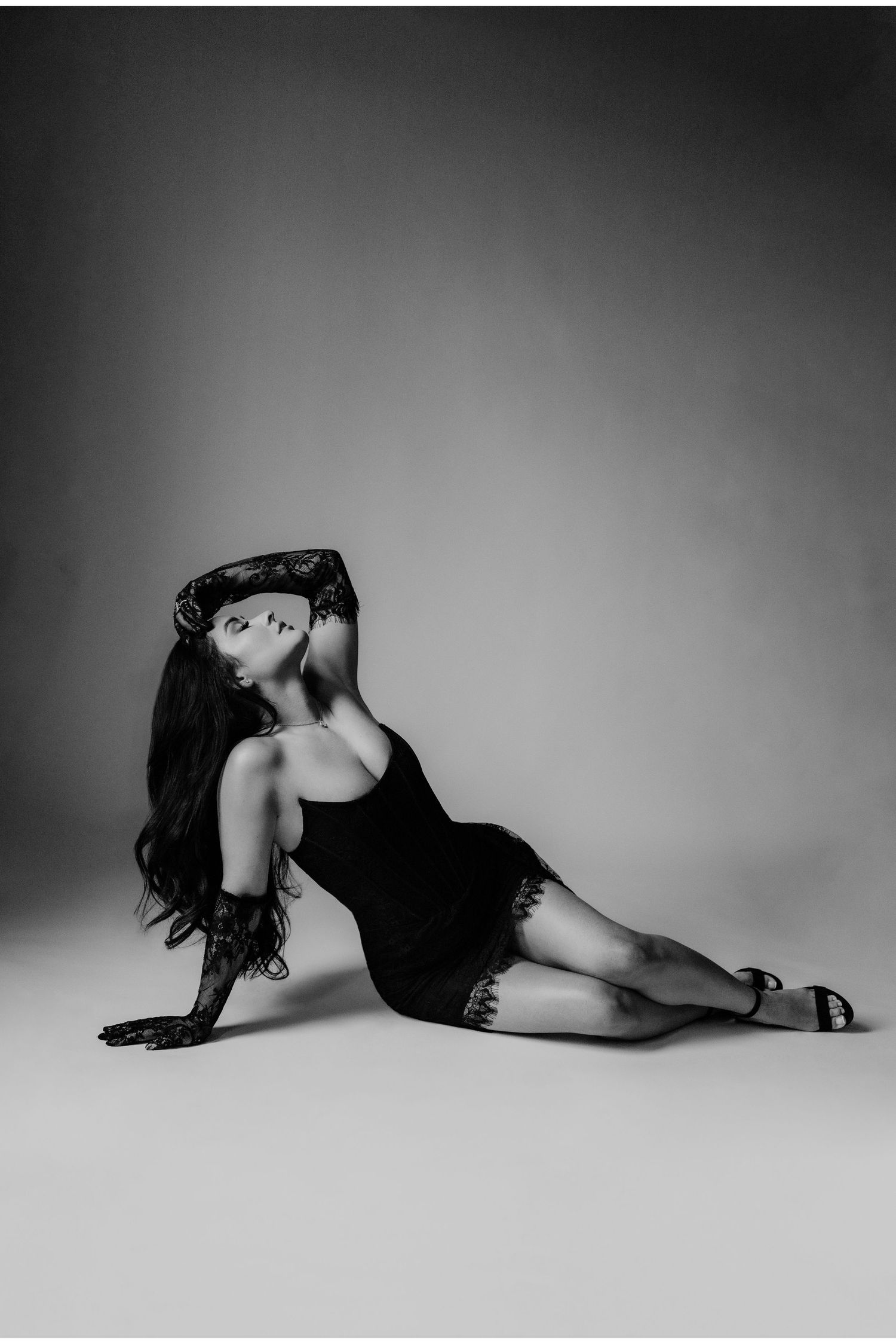 Black and white fashion portrait of model in black dress posing on floor.