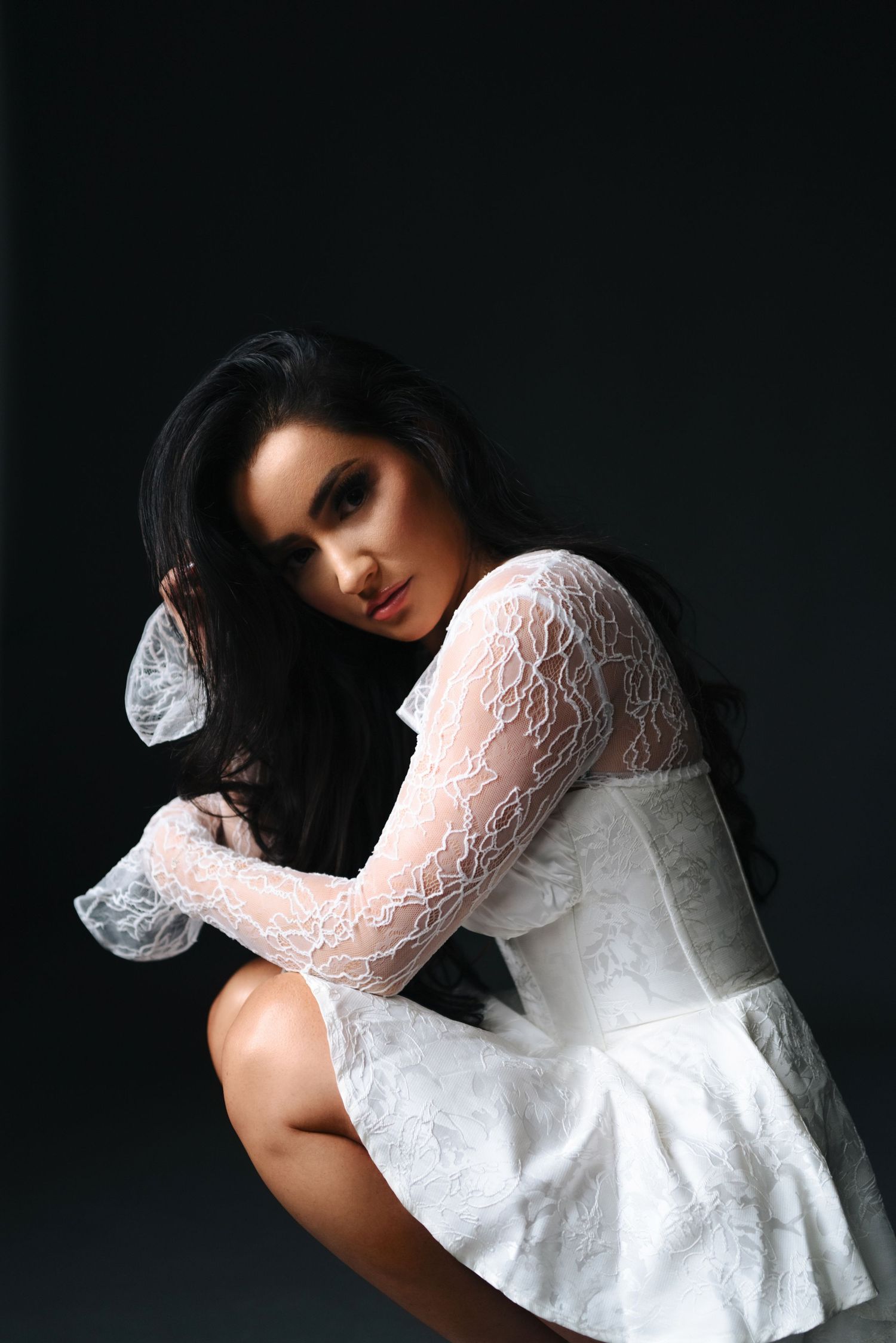 Romantic portrait of model in white lace dress against dark background.