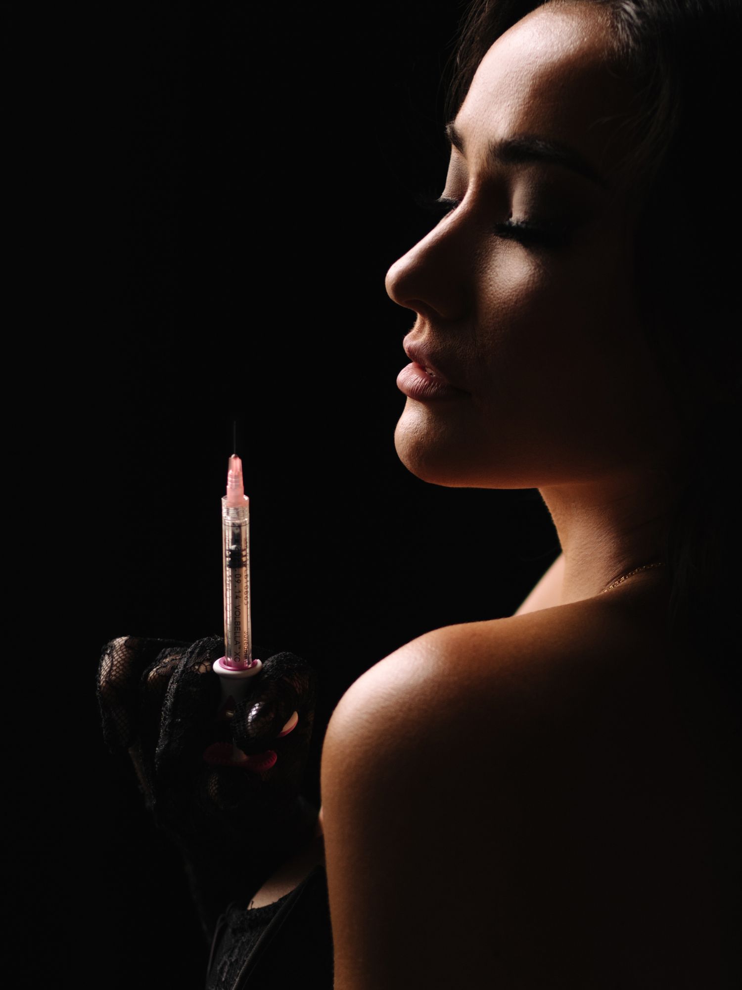 Artistic low-key portrait showing profile view of figure holding a glowing lipstick in dark lighting.