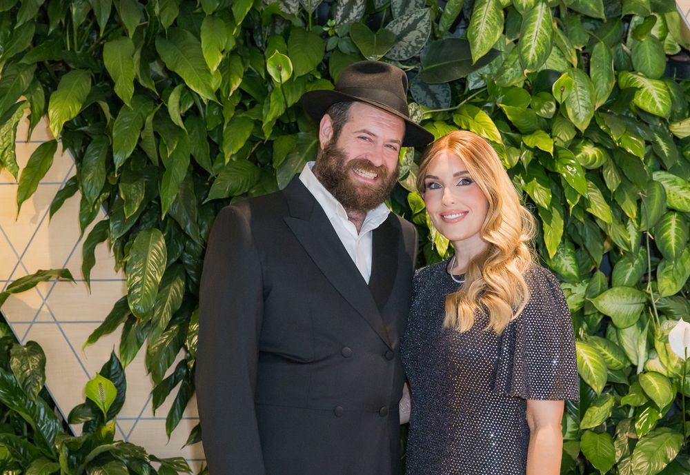 Two people pose together in front of a green ivy wall during a formal event.