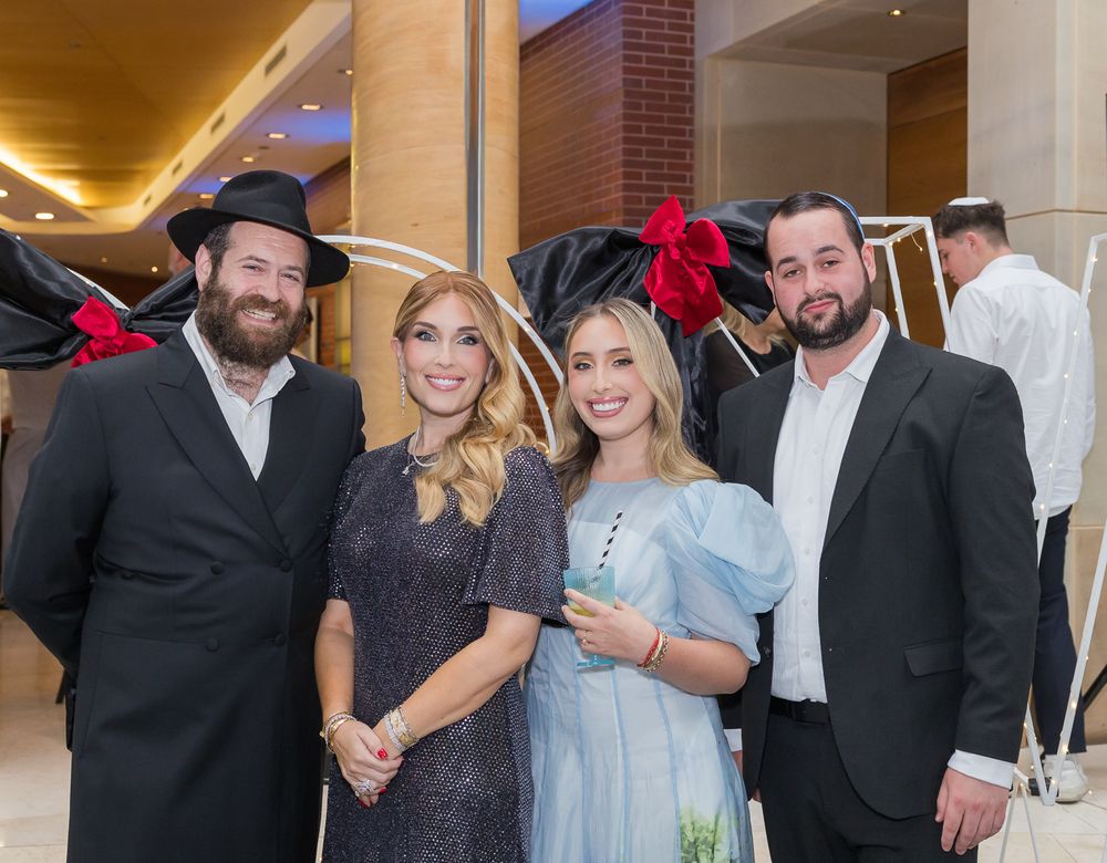 Group of people gathered at an indoor event wearing formal attire including suits and dresses.