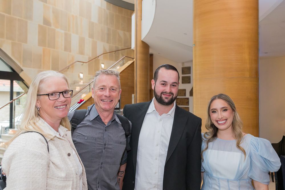 A group of people gather and smile together in an elegant indoor setting with wooden columns.