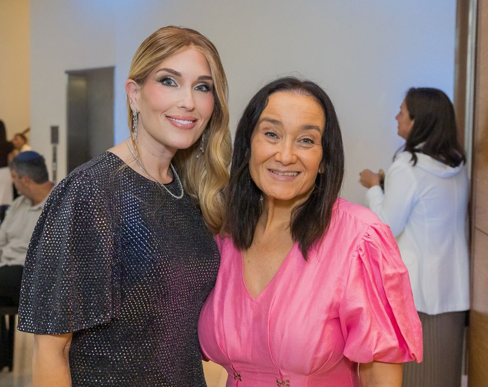 Two women pose together at an event, one wearing a navy polka dot dress and the other in a bright pink dress.