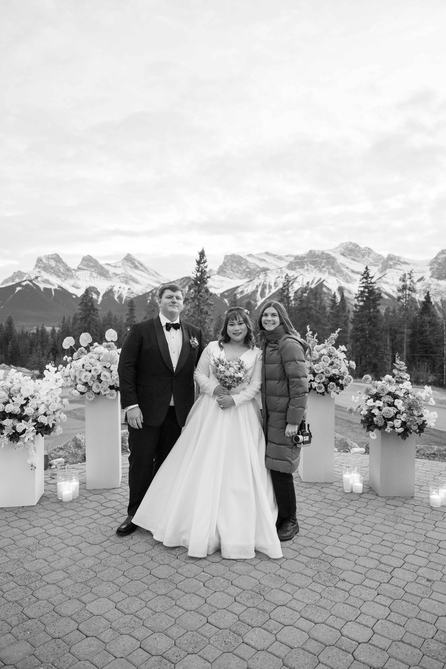 A winter wedding ceremony on a stone patio with snow-capped mountains and evergreen trees in the background.