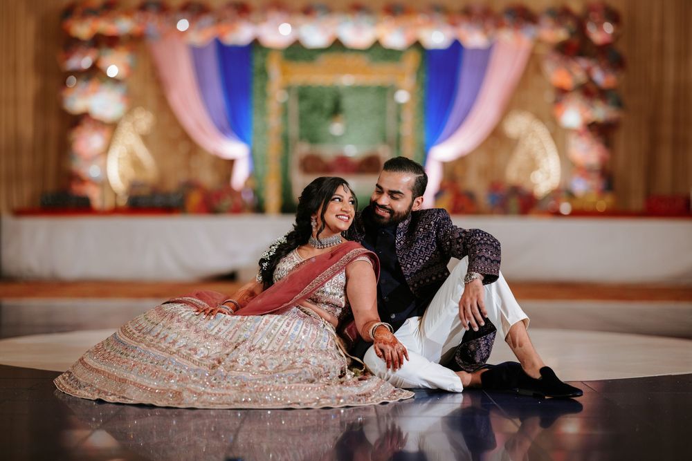 Couple in elegant attire lying on polished dance floor at wedding reception venue.