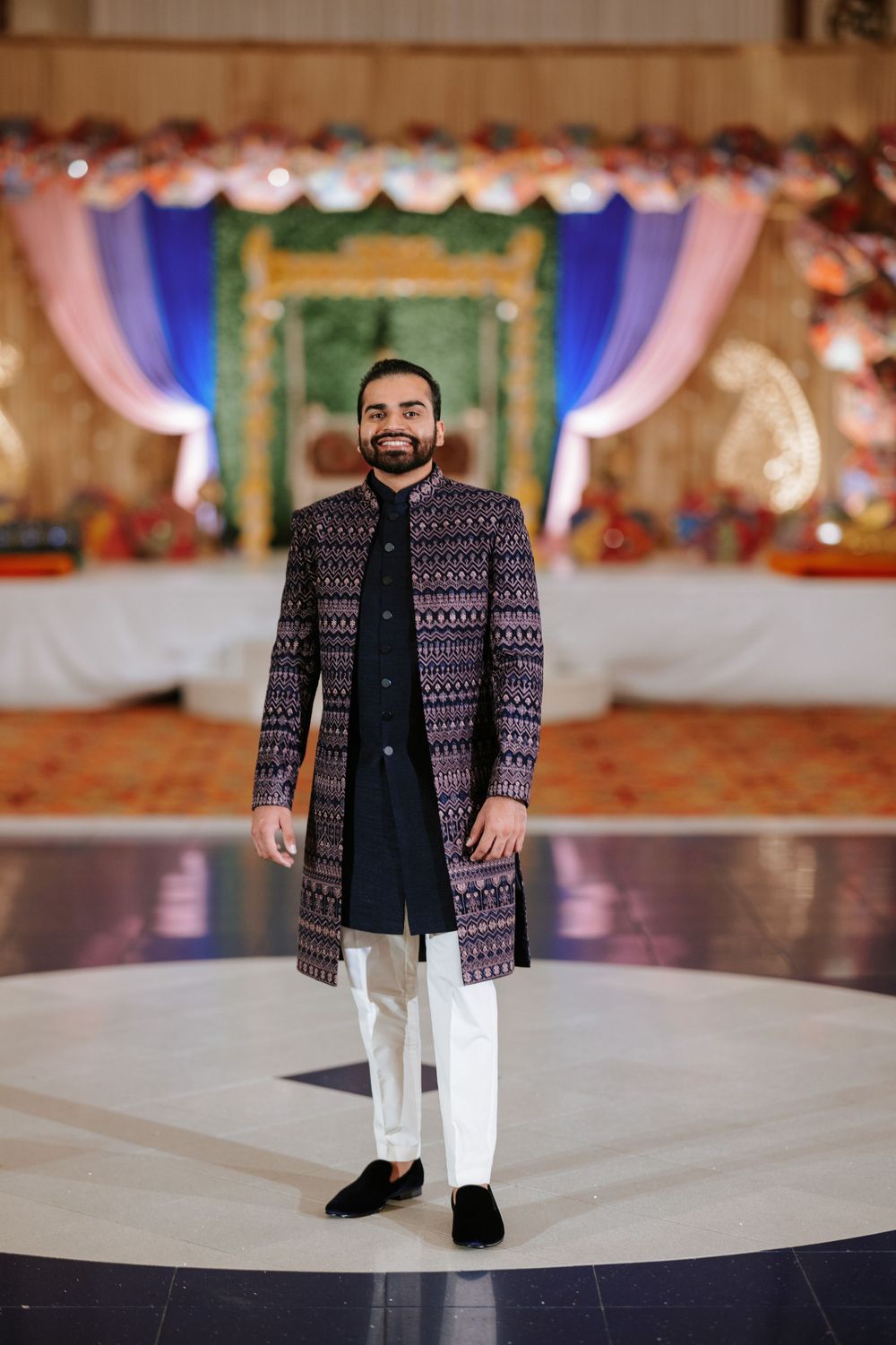 Person wearing a patterned navy jacket with white pants stands on a light-colored platform at a formal event.