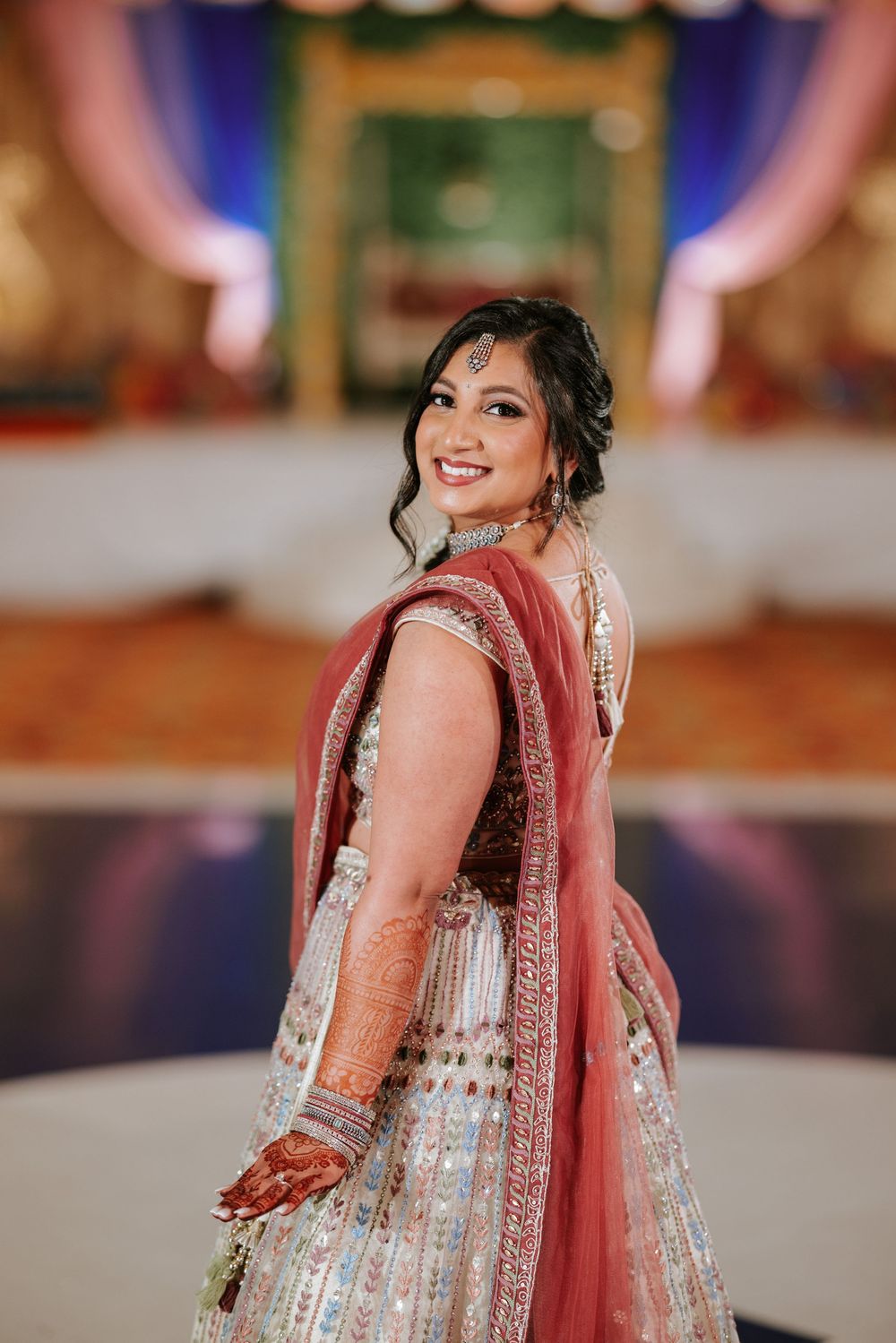 A person wearing an ornate white and red Indian lehenga poses elegantly at a wedding celebration.