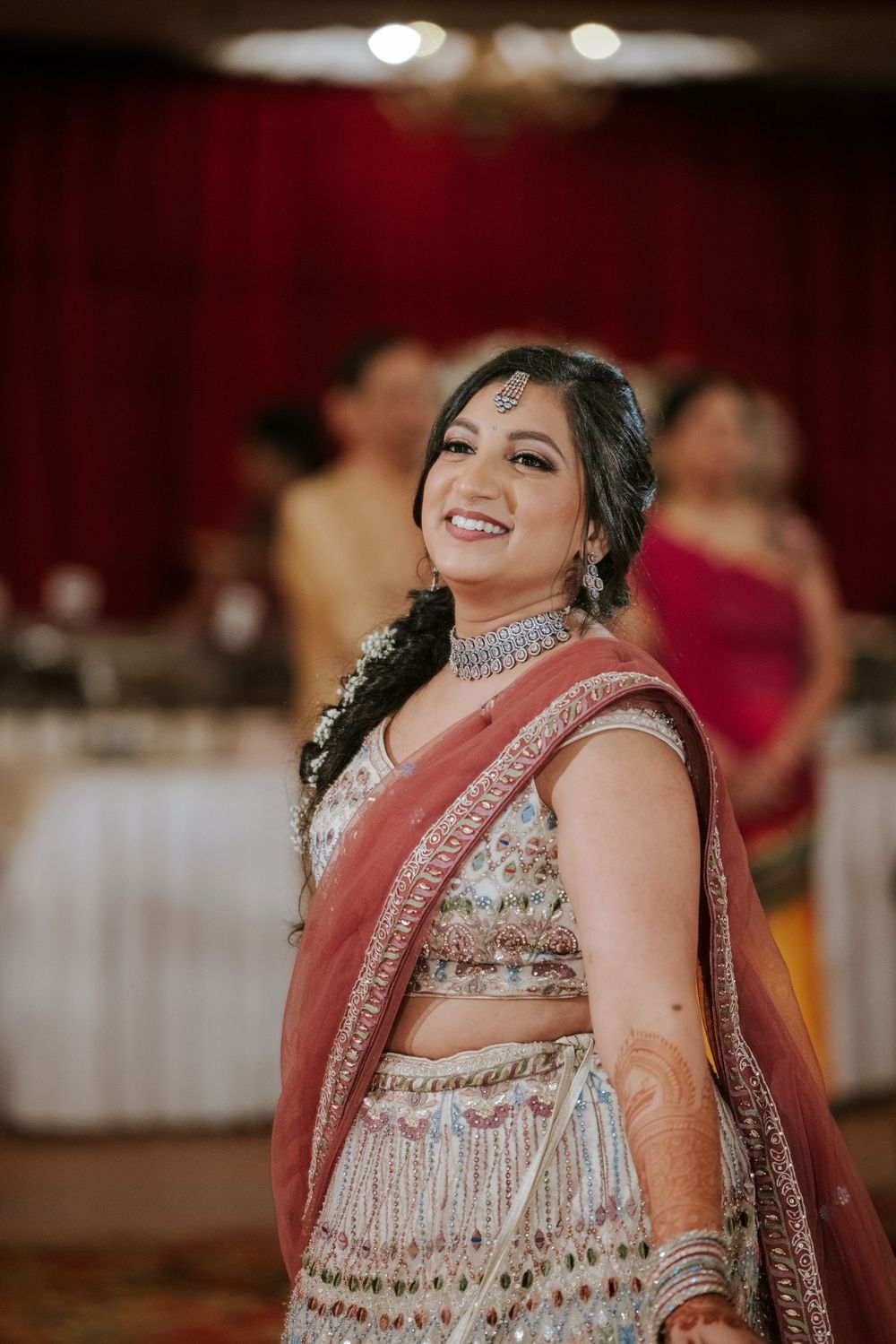 Bride in traditional Indian wedding attire with intricate embroidery and jewels smiling at reception venue.