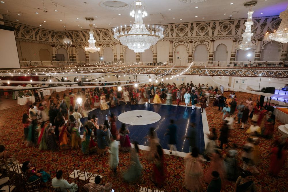 Large ballroom filled with wedding guests dancing under ornate chandeliers at an elegant reception.
