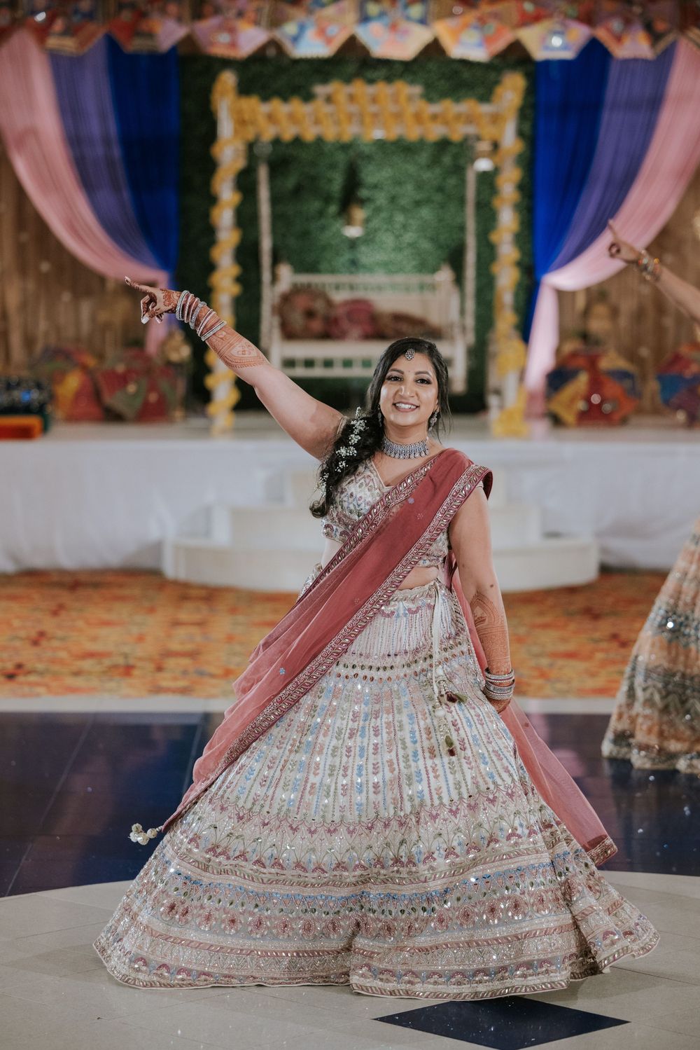 A dancer in an ornate white and pink lehenga performs a graceful twirl on a decorated stage.