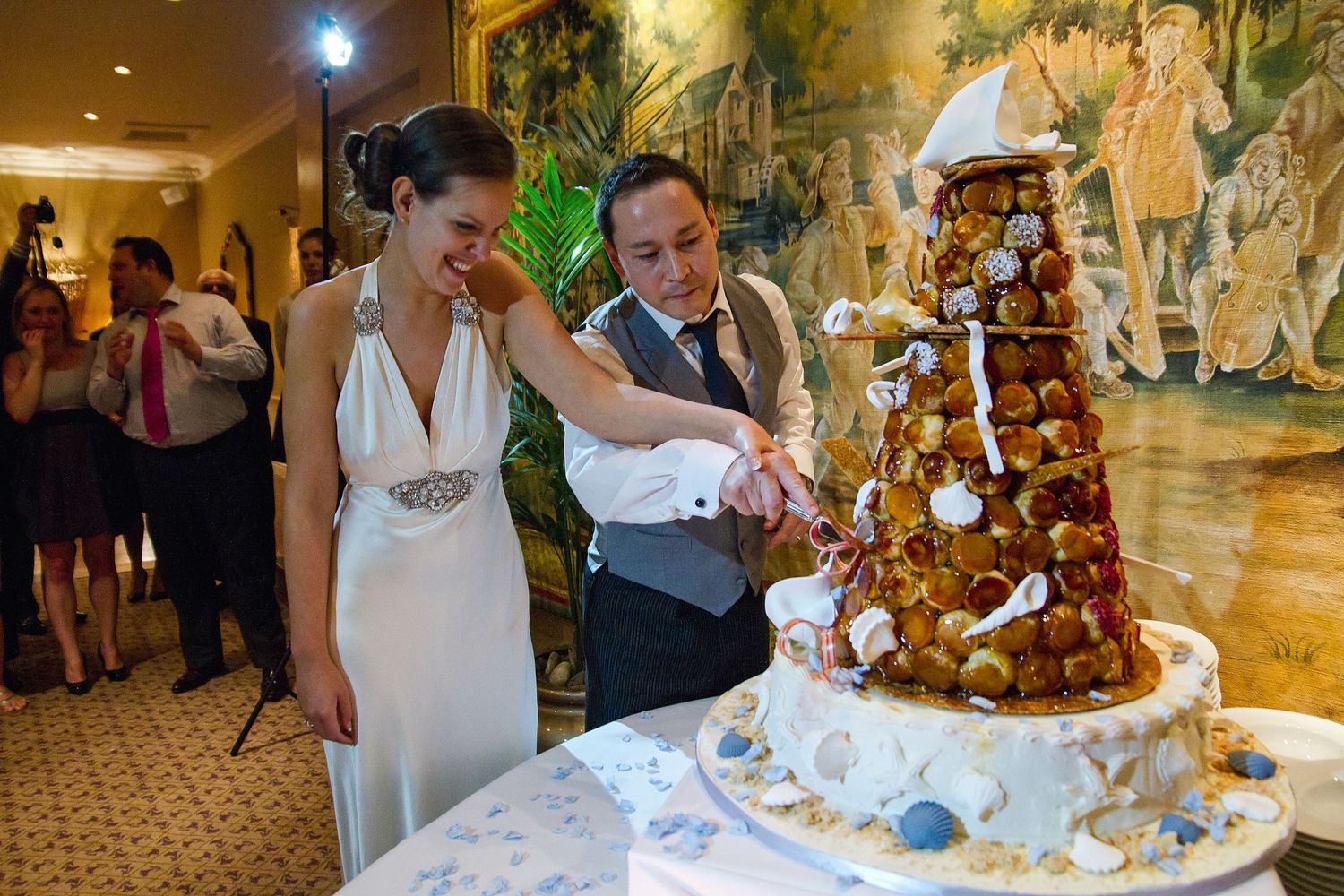 Wedding reception guests gather around an elegant croquembouche dessert tower decorated with caramel and flowers.