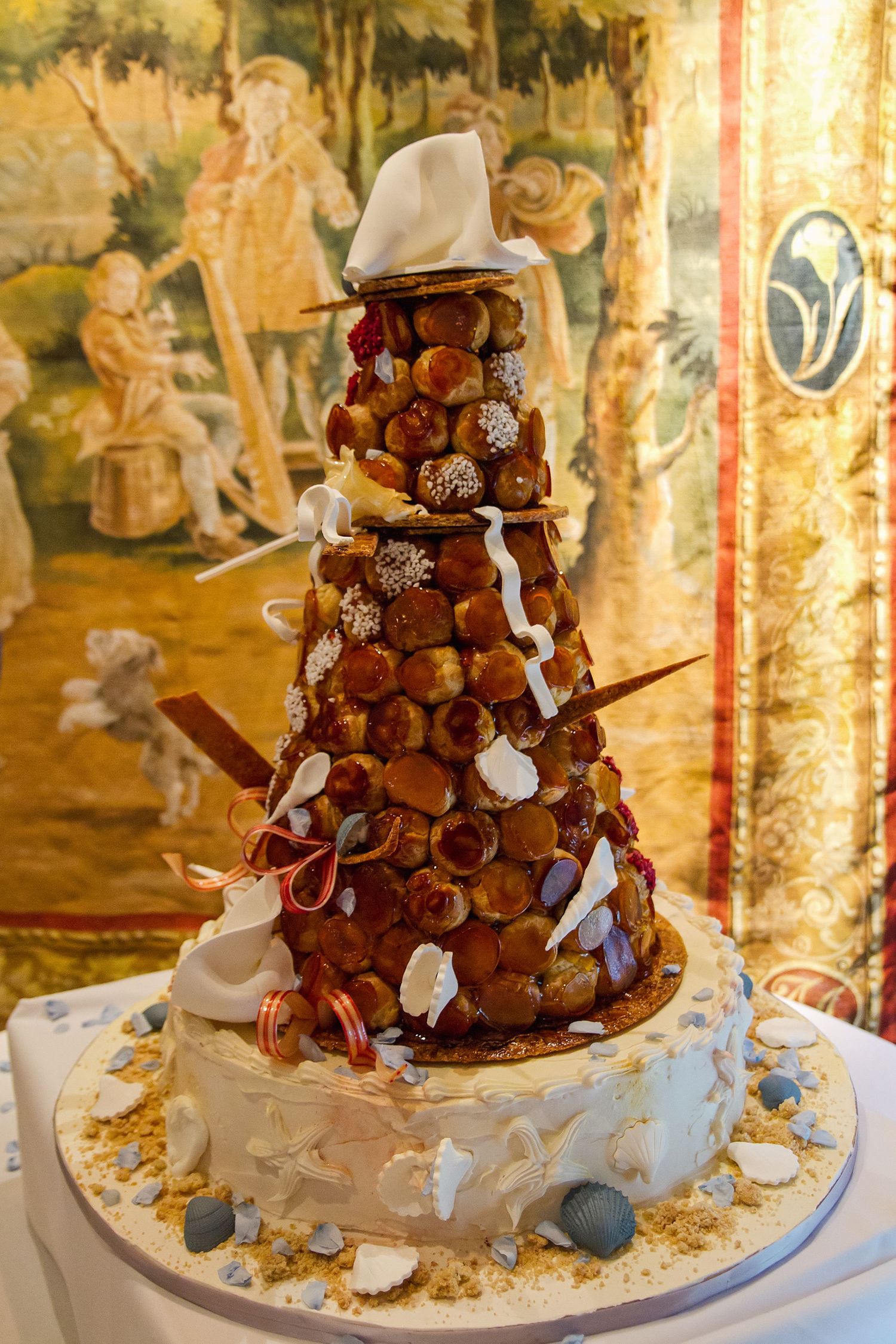 A chocolate croquembouche tower decorated with white ribbons and butterflies sits elegantly on a dessert table.