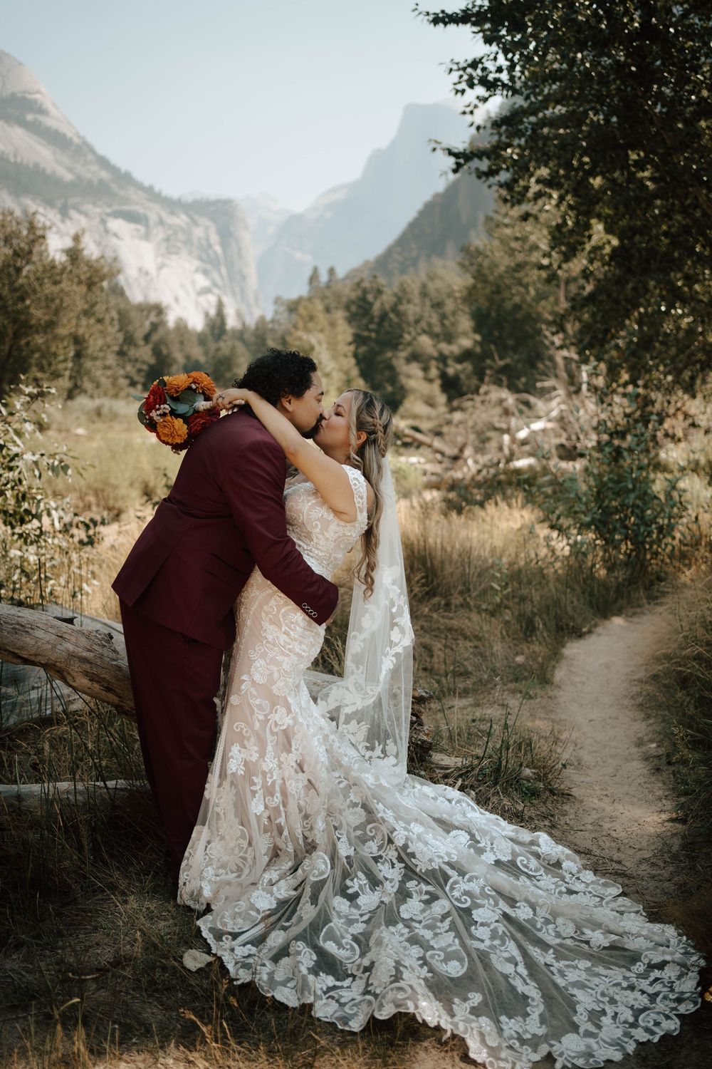 Couple sharing a kiss in Yosemite Valley with bride in lace gown holding autumn floral bouquet.