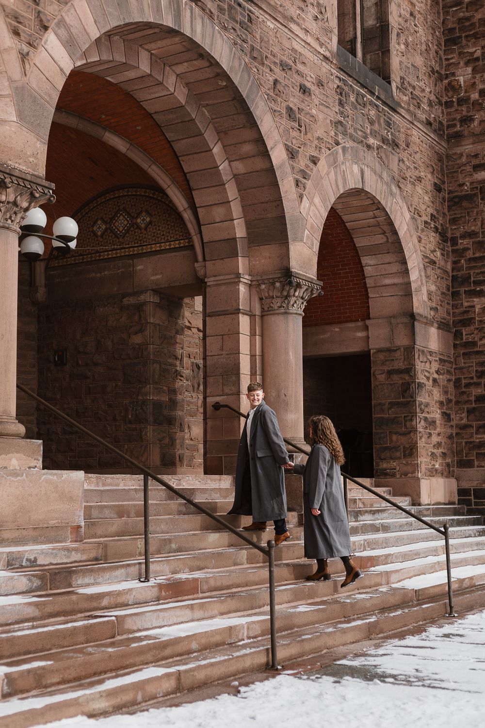 Couple walking through a series of stone archways in an historic building with brick walls and stone steps.