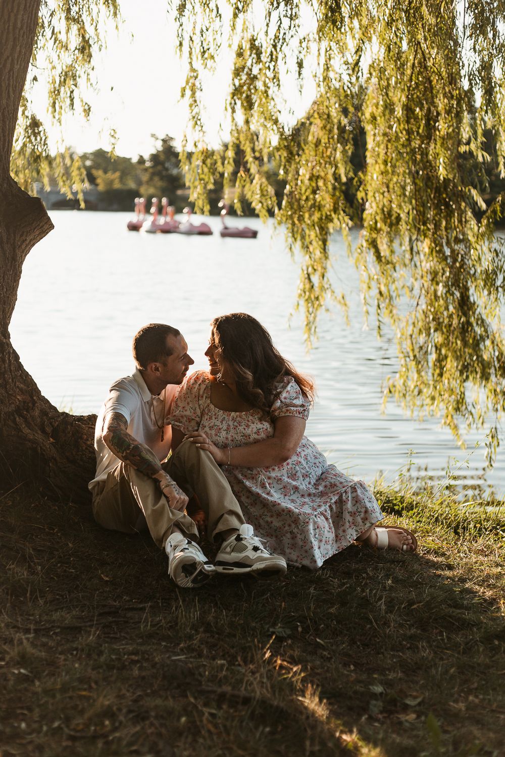 A couple sits together under a weeping willow tree by a serene lake during golden hour.