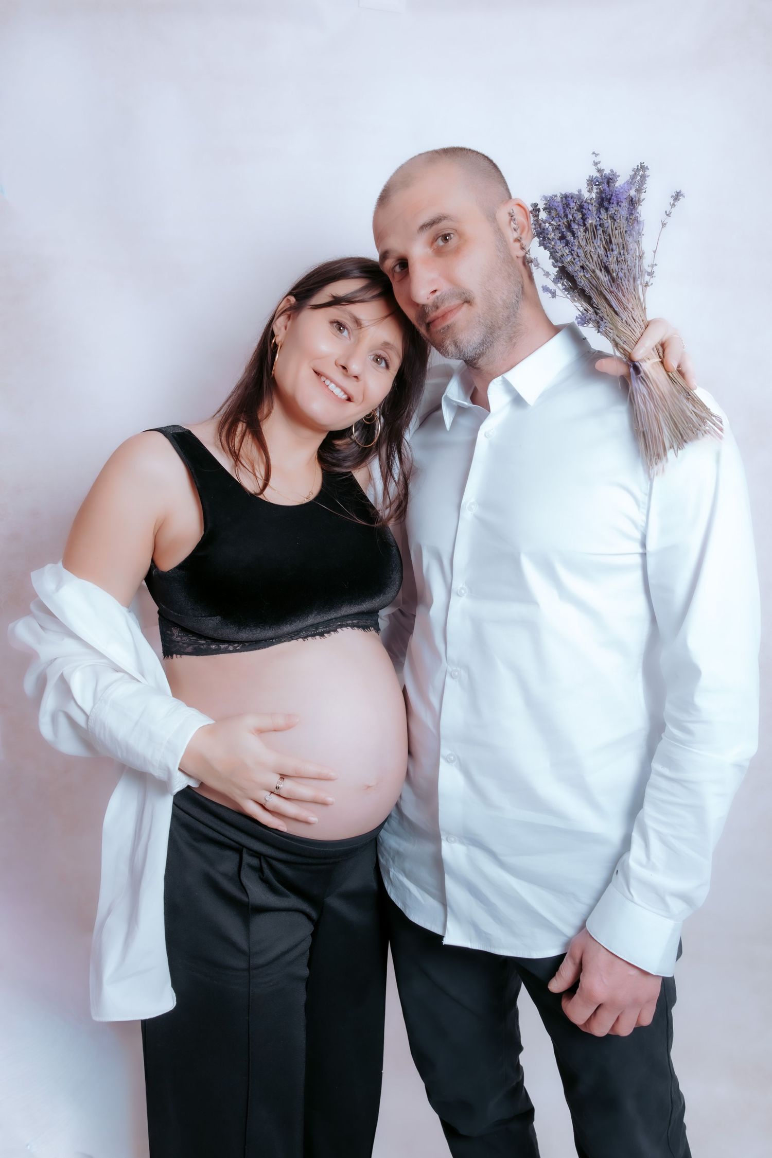 A couple in black and white outfits pose together in a series of intimate maternity photos against a light background.