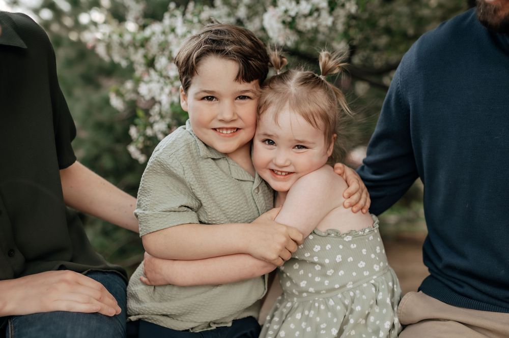Young boy and girl hugging each other in front of blooming spring trees.