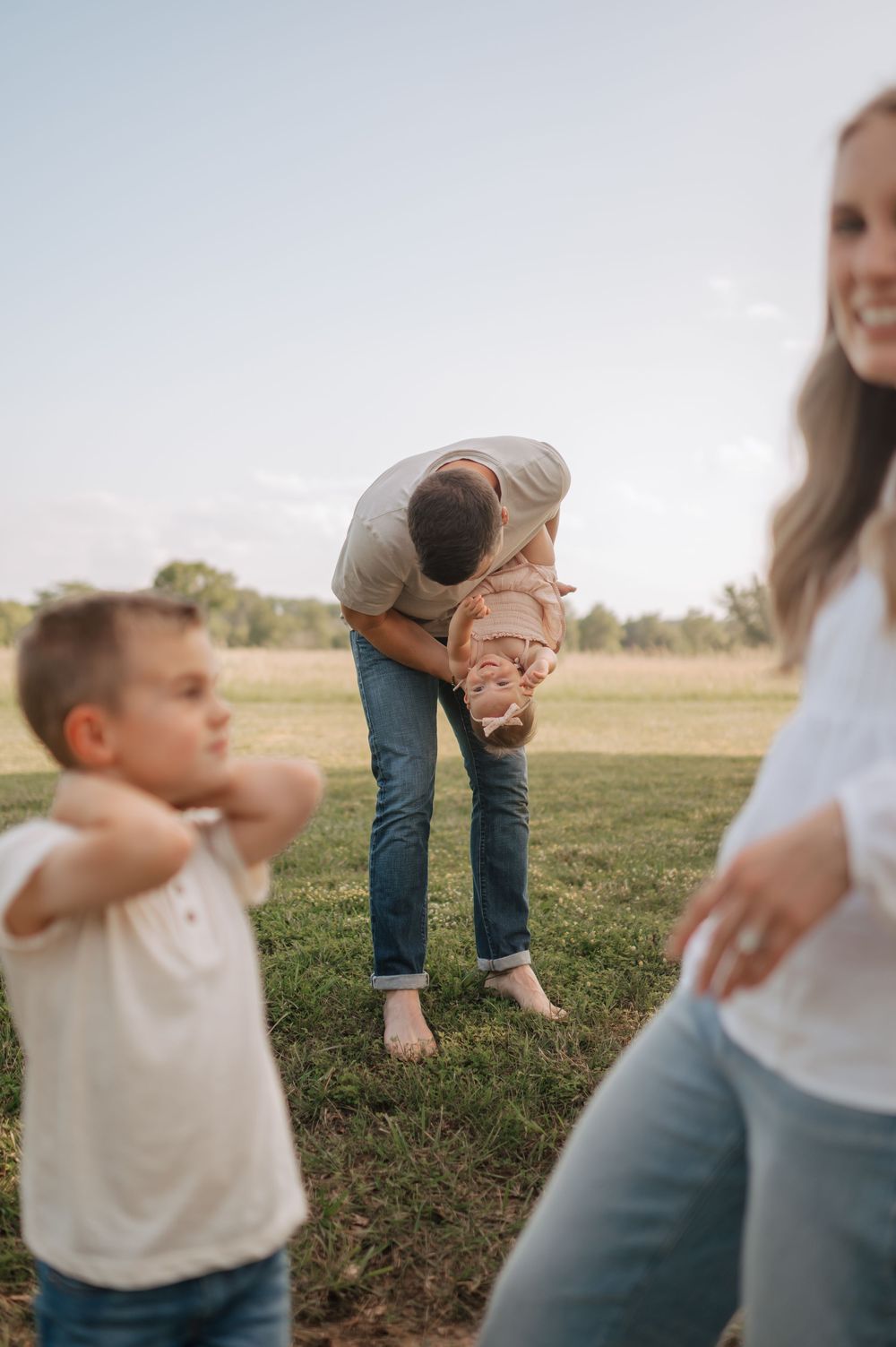 Father playfully lifting child upside down in grassy field at sunset.