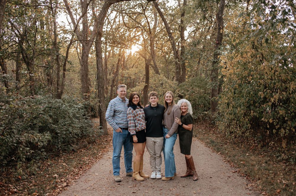 Family of five smiling together on a wooded path during golden hour autumn sunset.