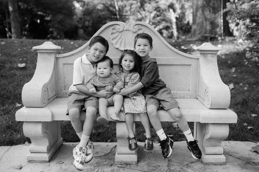 Four Asian children sitting together on an ornate stone bench in a park, black and white photo.