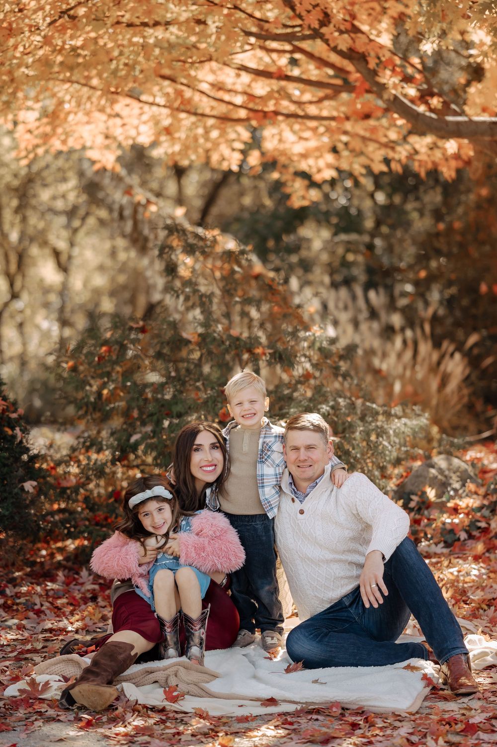 Family of four posing on blanket under colorful autumn trees.