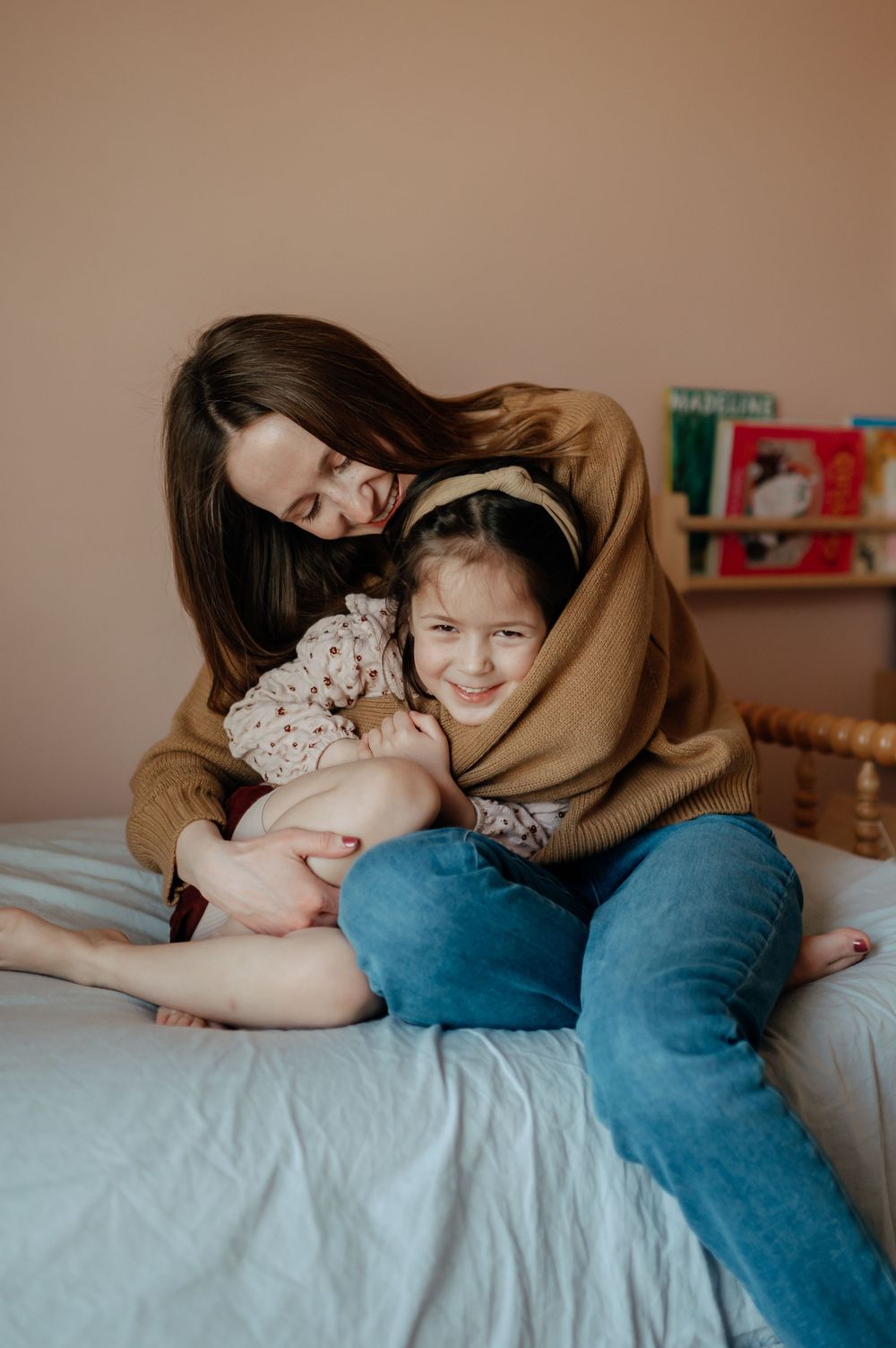 Mother hugging two young daughters on bed in cozy room.