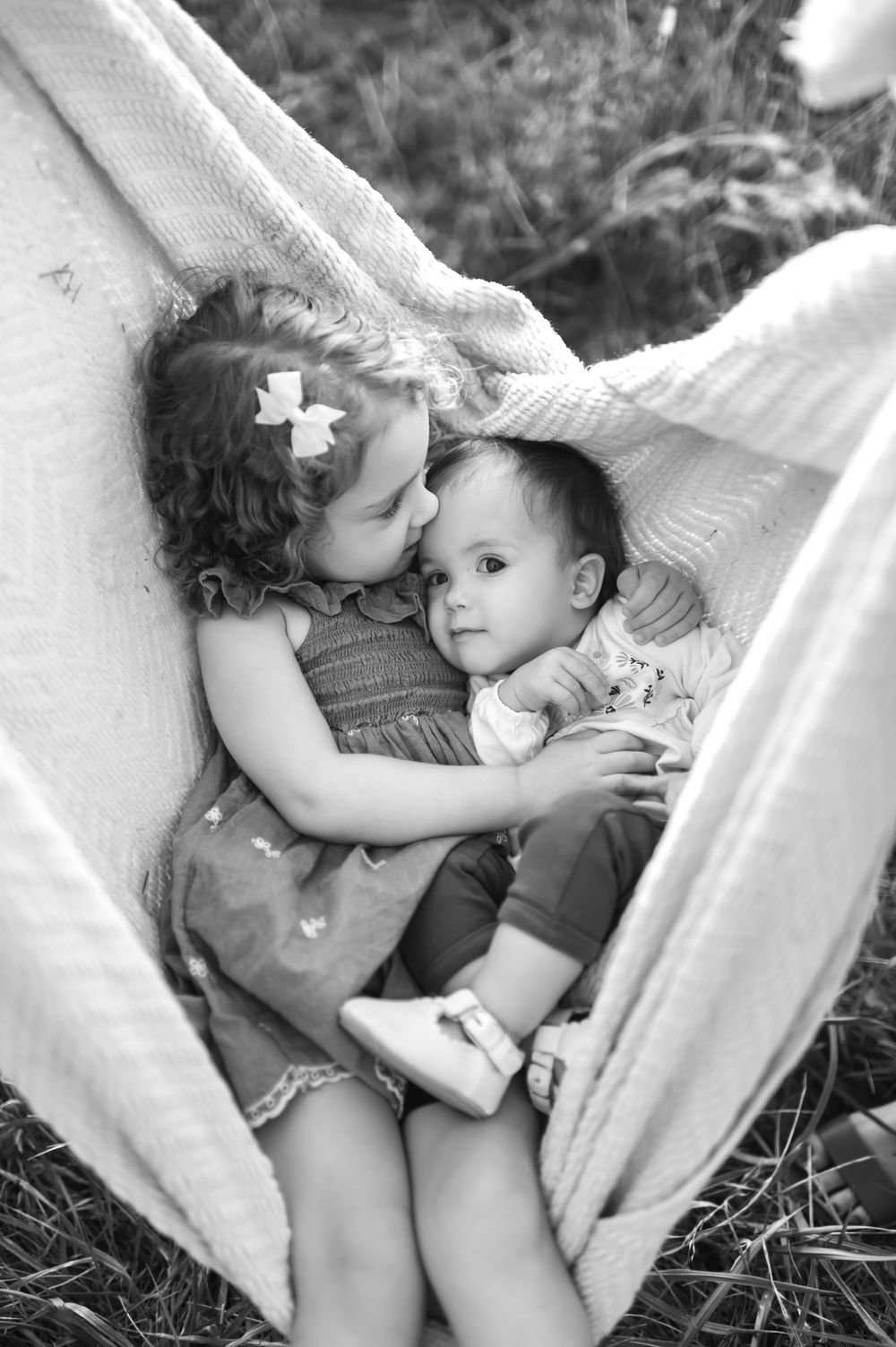 Black and white photo of young girl hugging baby in hammock.