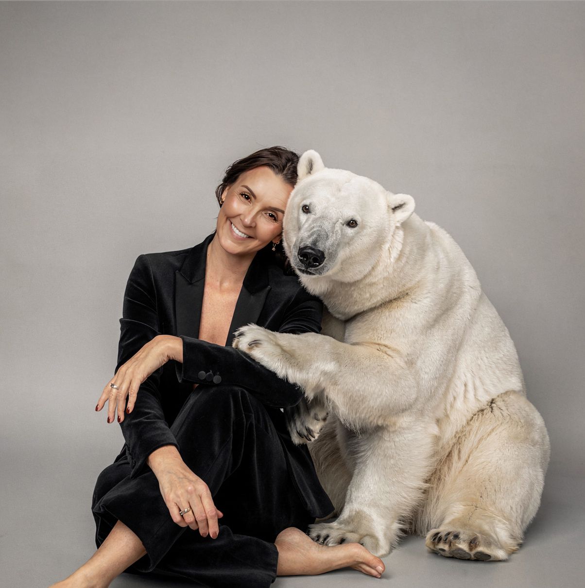 A person in black clothing poses with a large white polar bear figure against a gray studio backdrop.